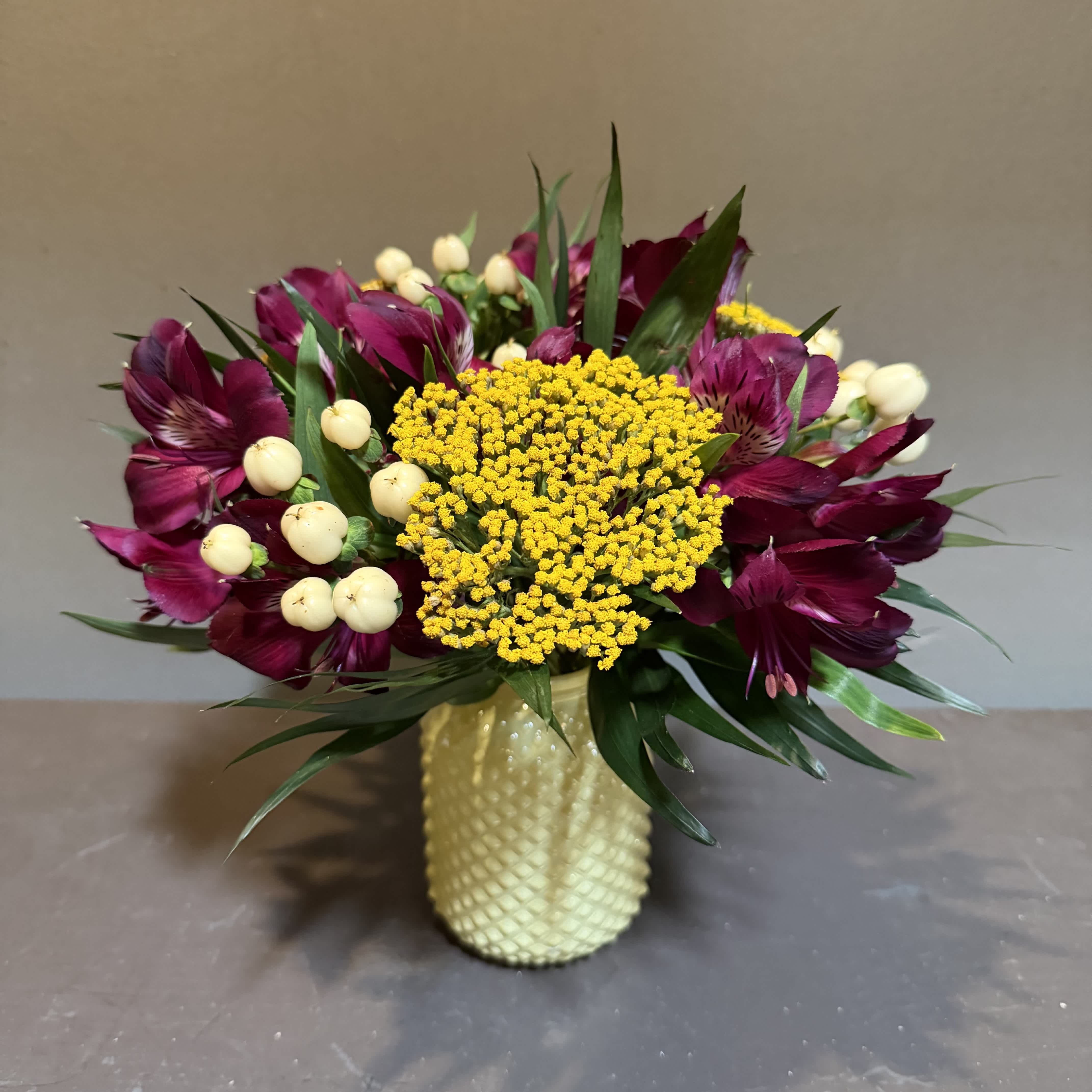 Bouquet of burgundy flowers with yellow blooms in a textured vase