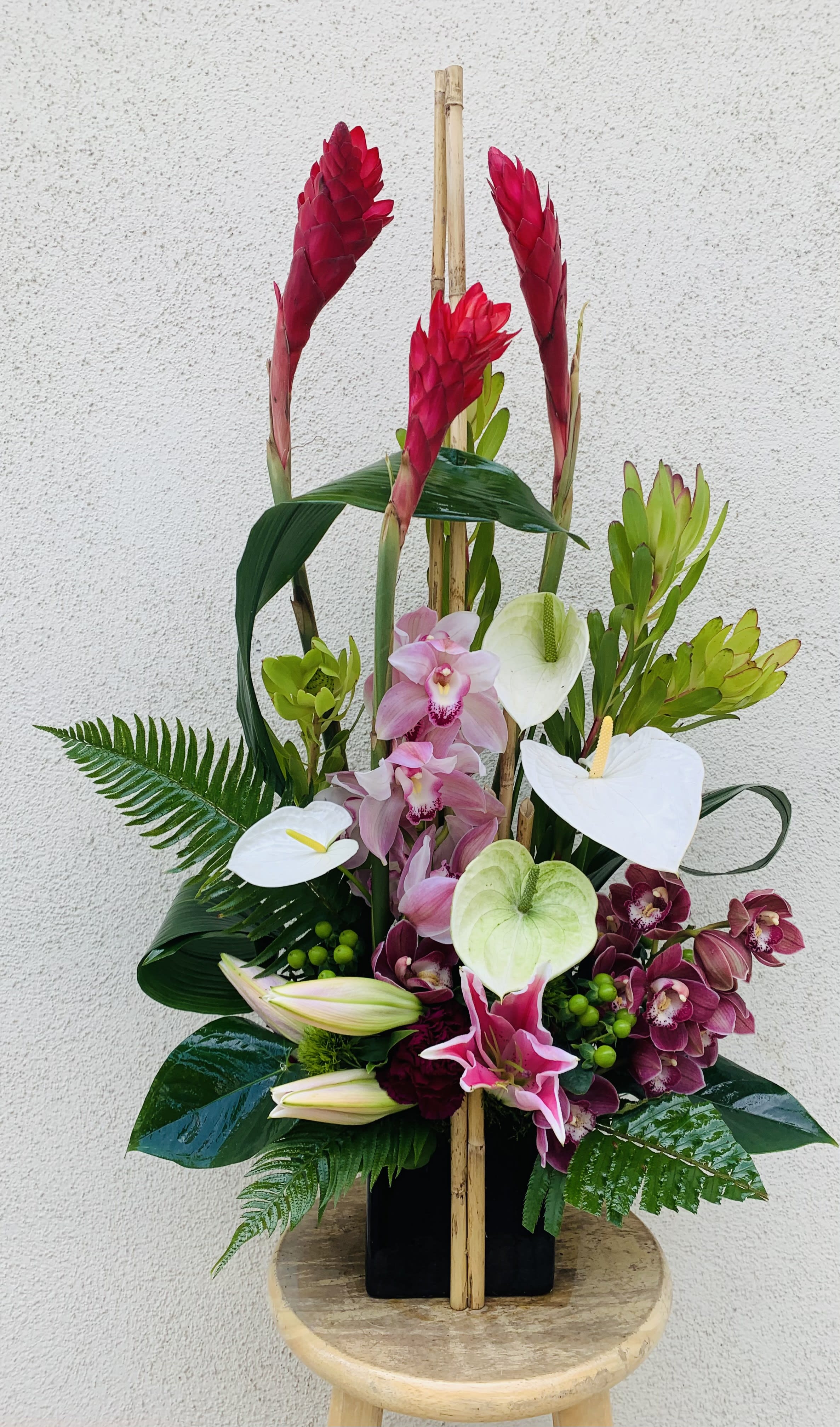 Tropical floral arrangement with pink orchids and white anthuriums in a black vase