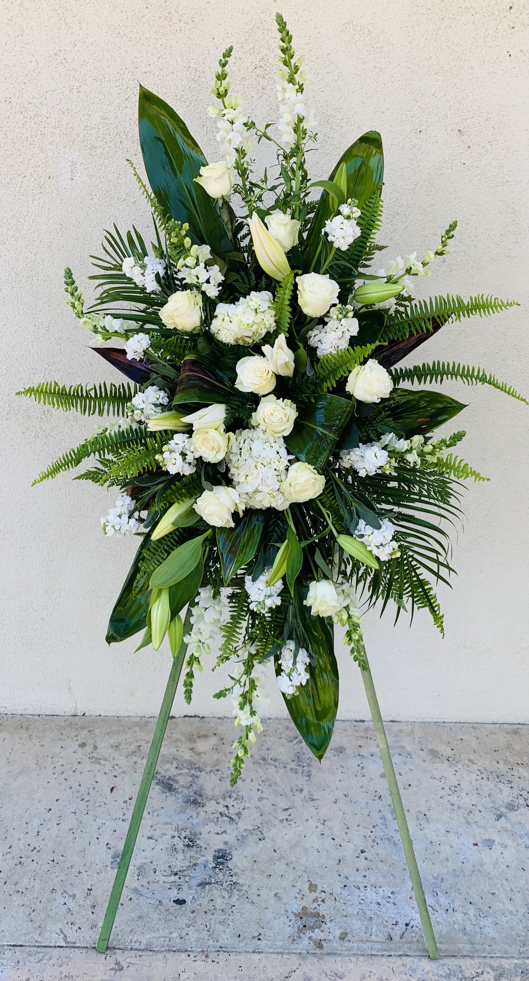 Tall white floral standing spray with roses and lilies on an easel