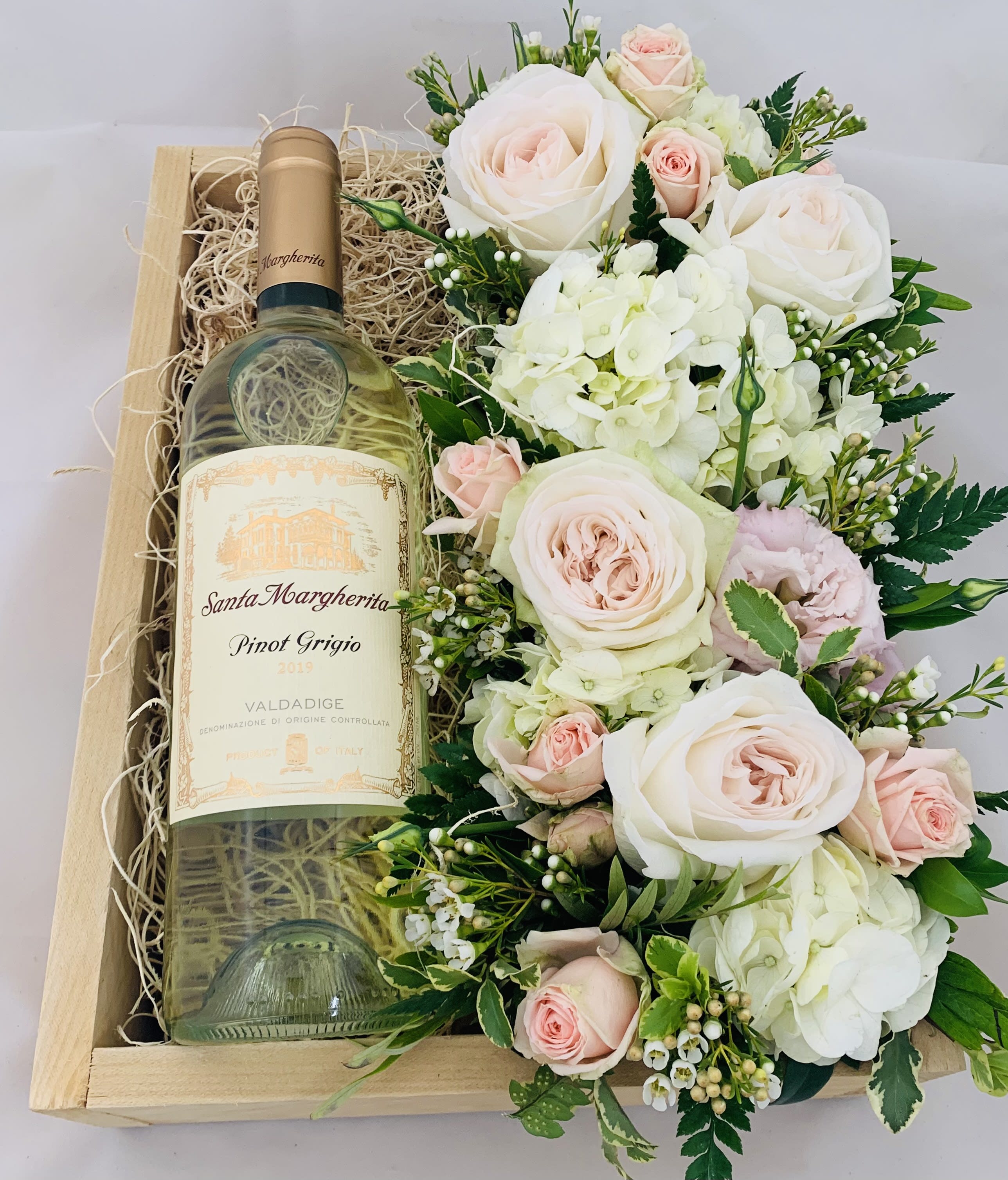 Wine bottle in a wooden gift box beside a pale pink and white flower arrangement