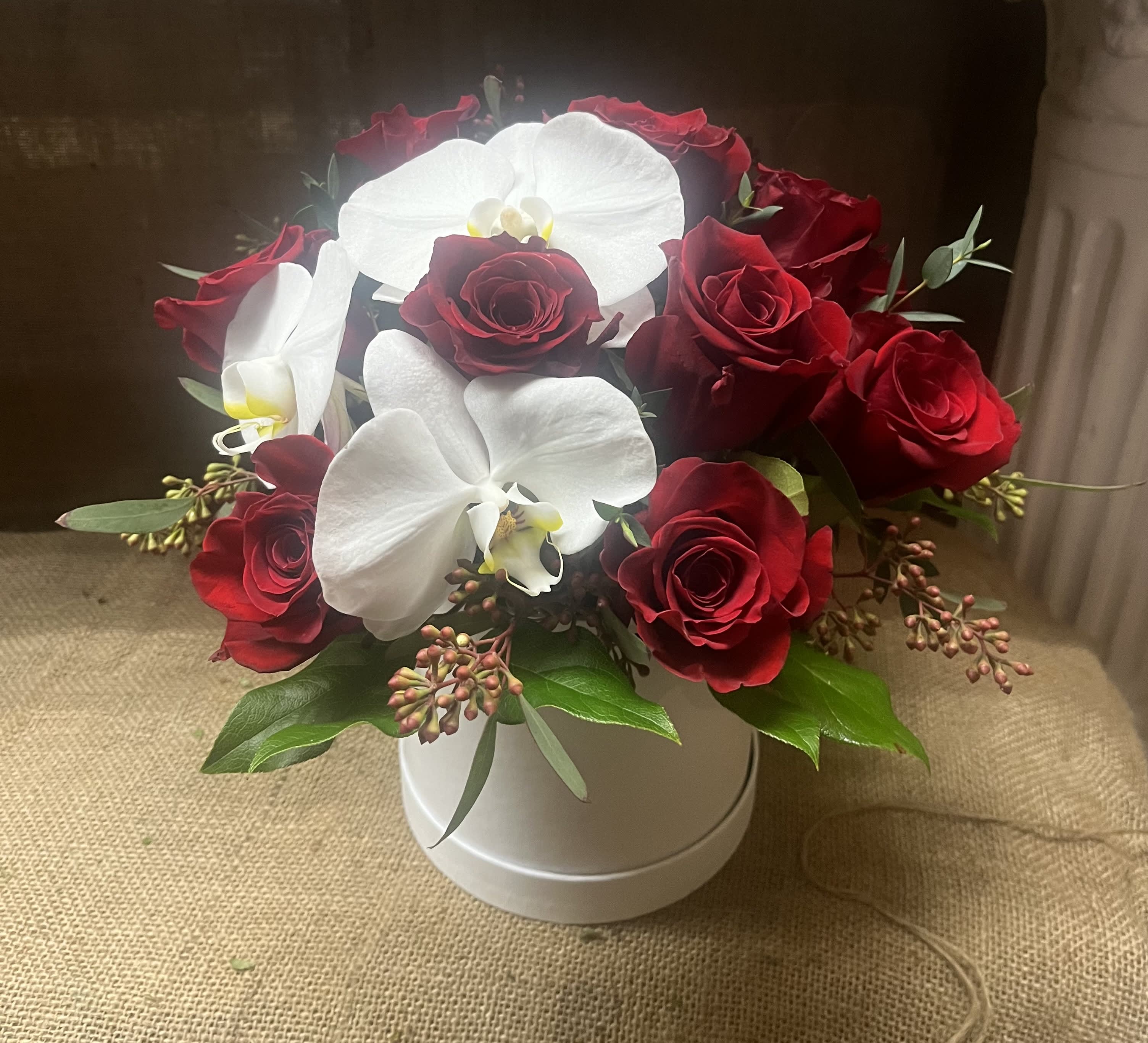 Red roses and white orchids arranged in a white hatbox