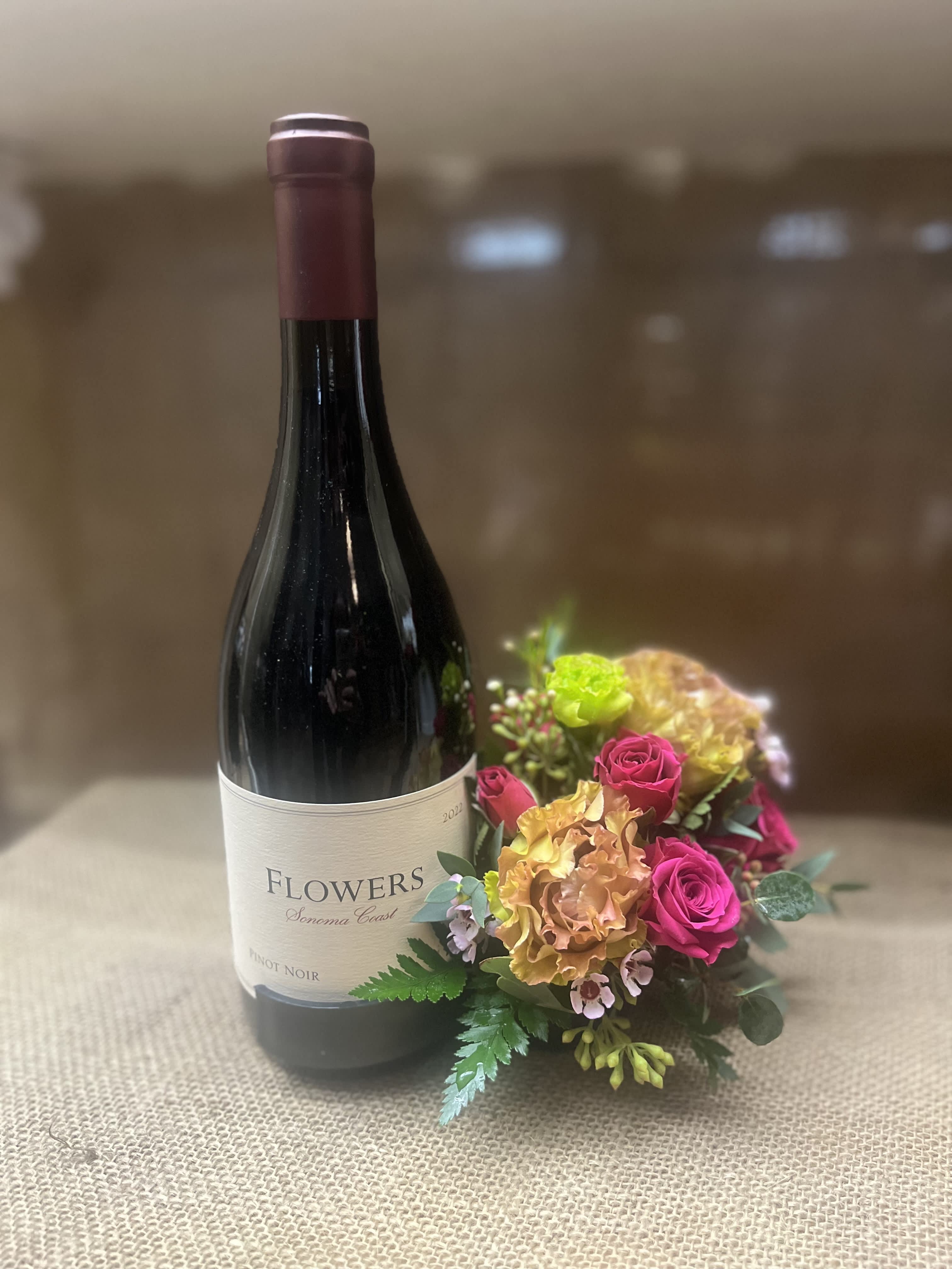 Wine bottle beside a small pink and peach floral arrangement