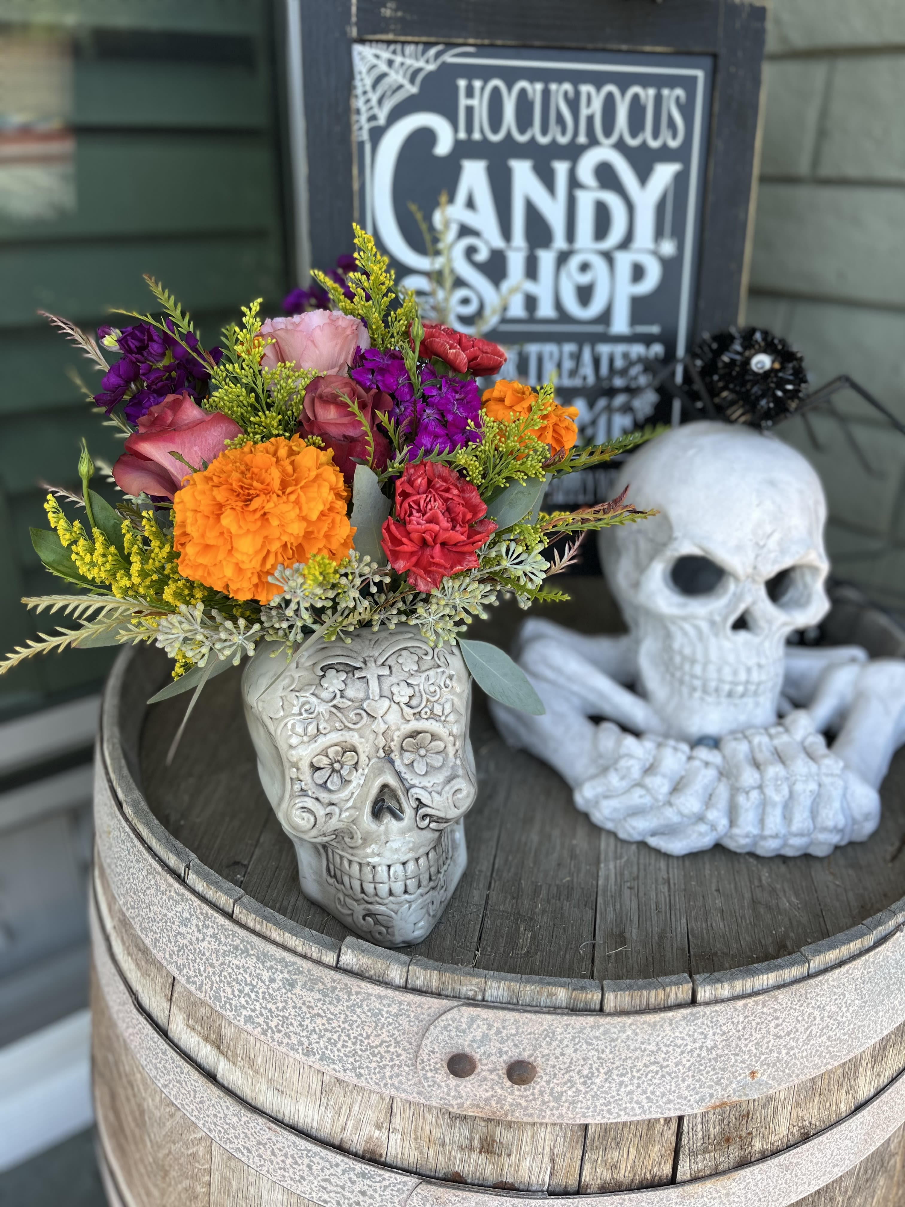 Colorful bouquet in a skull-shaped vase beside a decorative skull