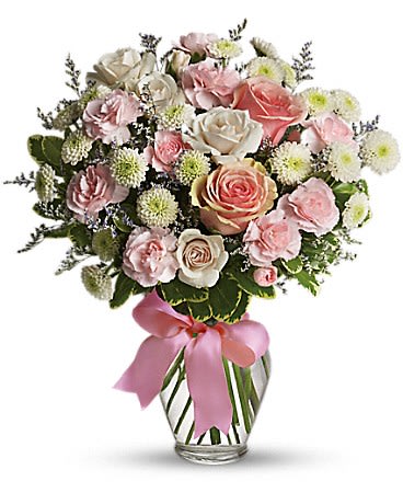 Pink and white rose bouquet in a clear glass vase with a pink ribbon