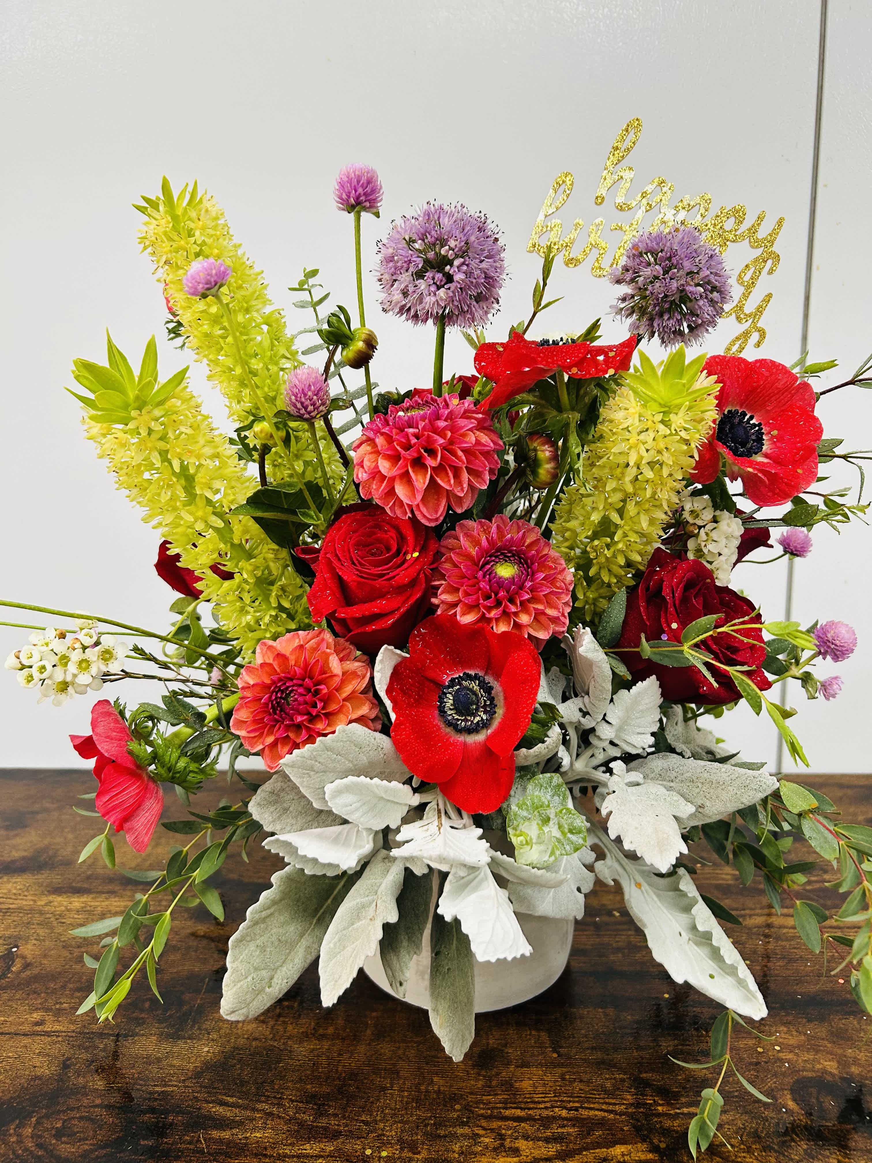 Bright mixed bouquet with red roses, pink dahlias, and purple blooms in a white vase