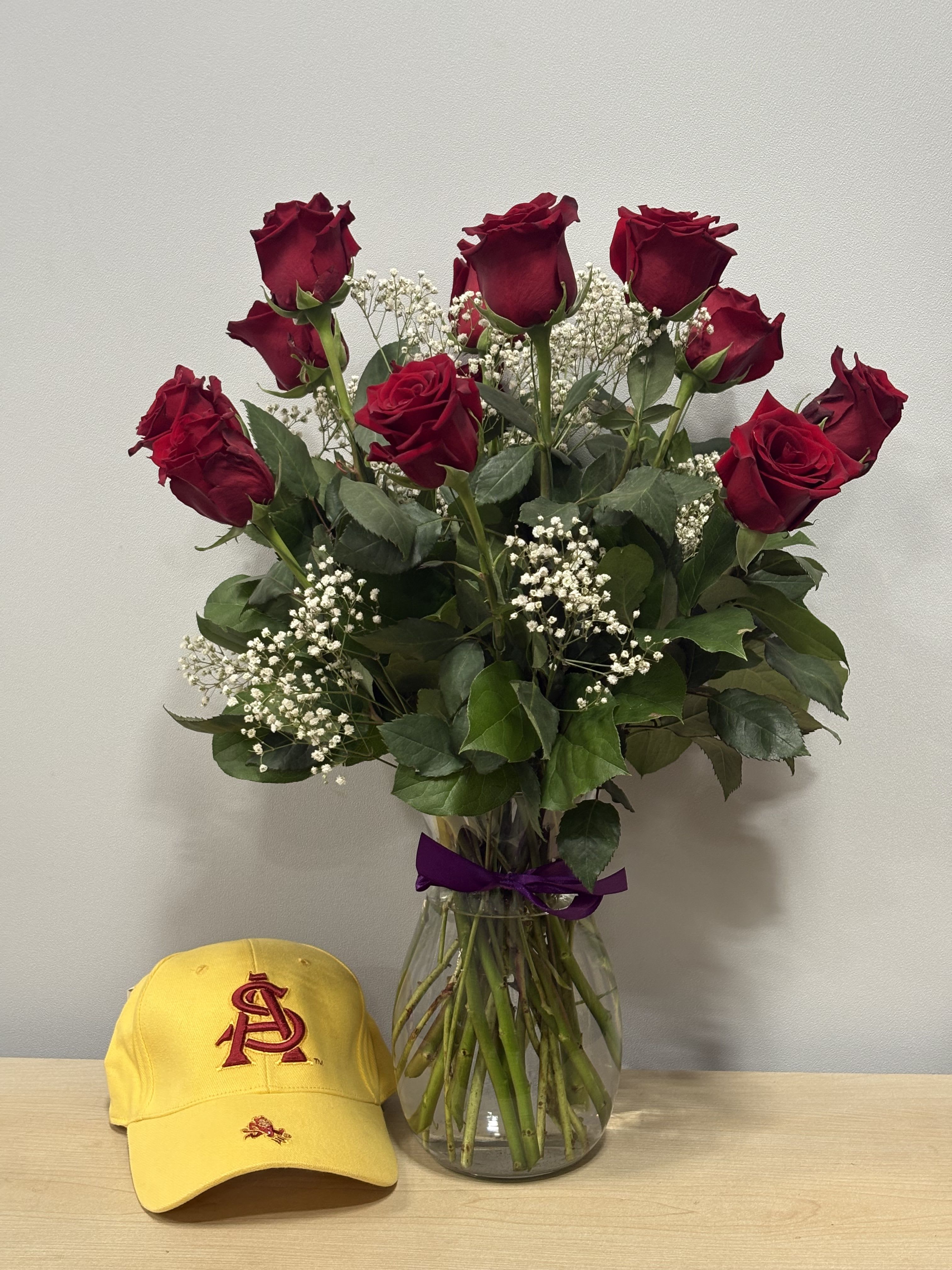 Bouquet of red roses in a glass vase with a yellow cap beside it.