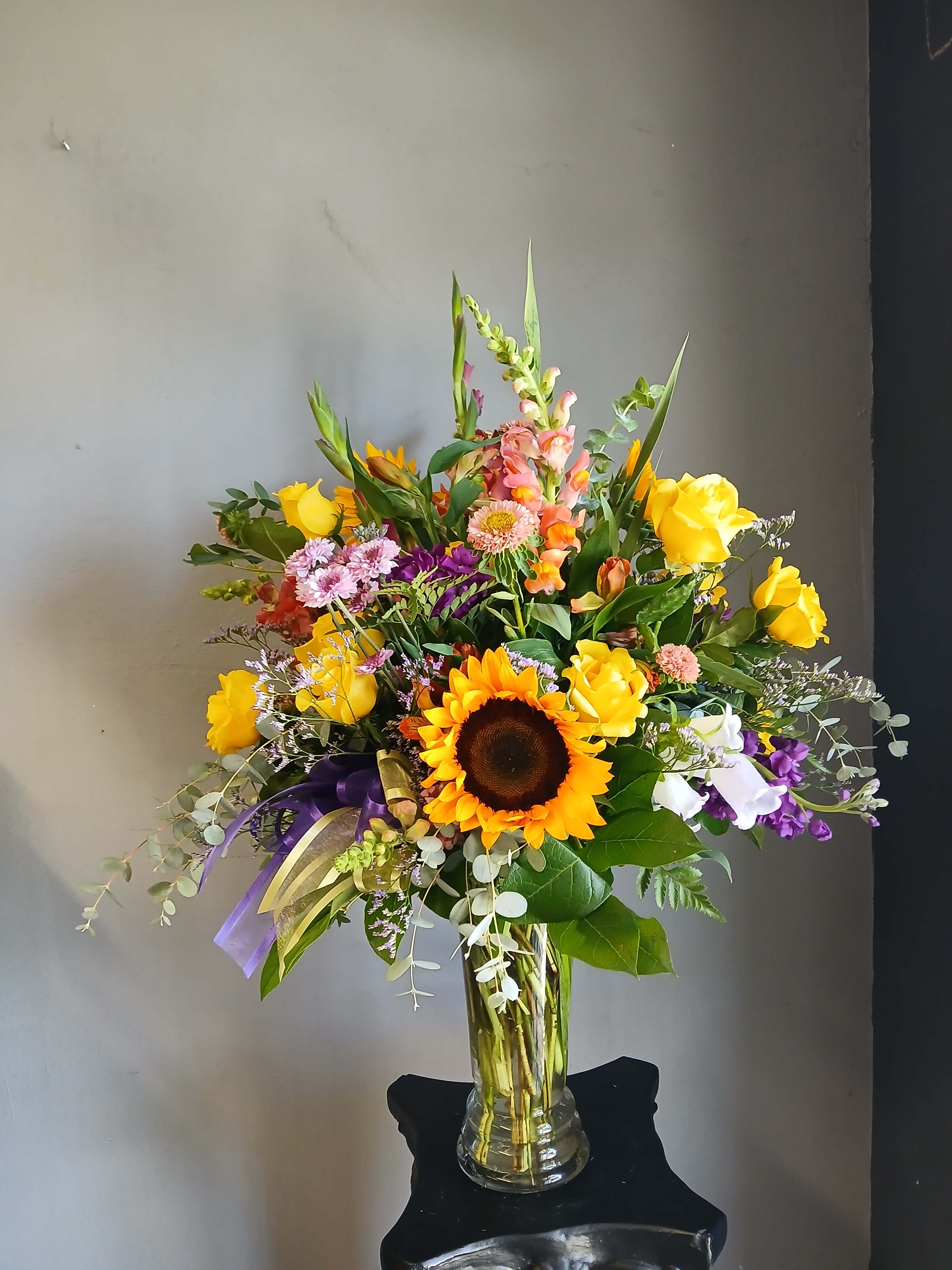 Mixed bouquet with sunflowers, yellow roses, and purple flowers in a glass vase