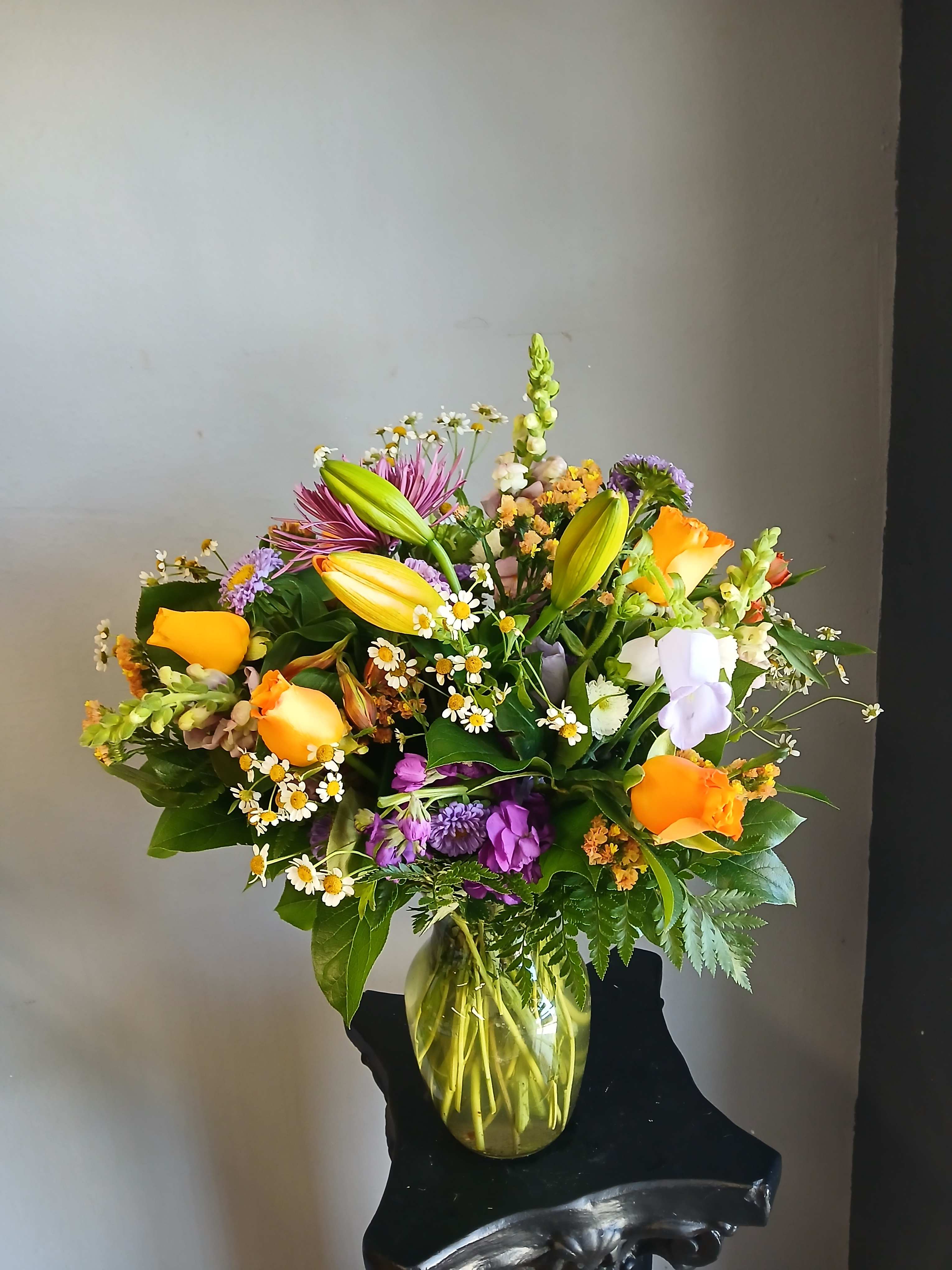 Mixed bouquet of lilies, roses, and purple flowers in a glass vase