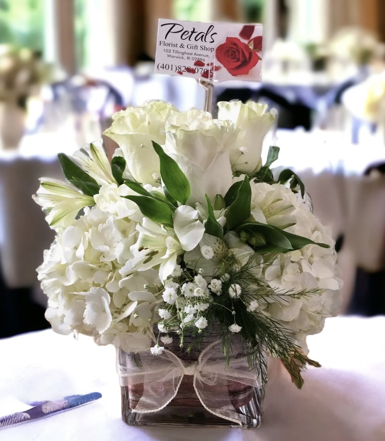 White floral arrangement in a square glass vase with a ribbon