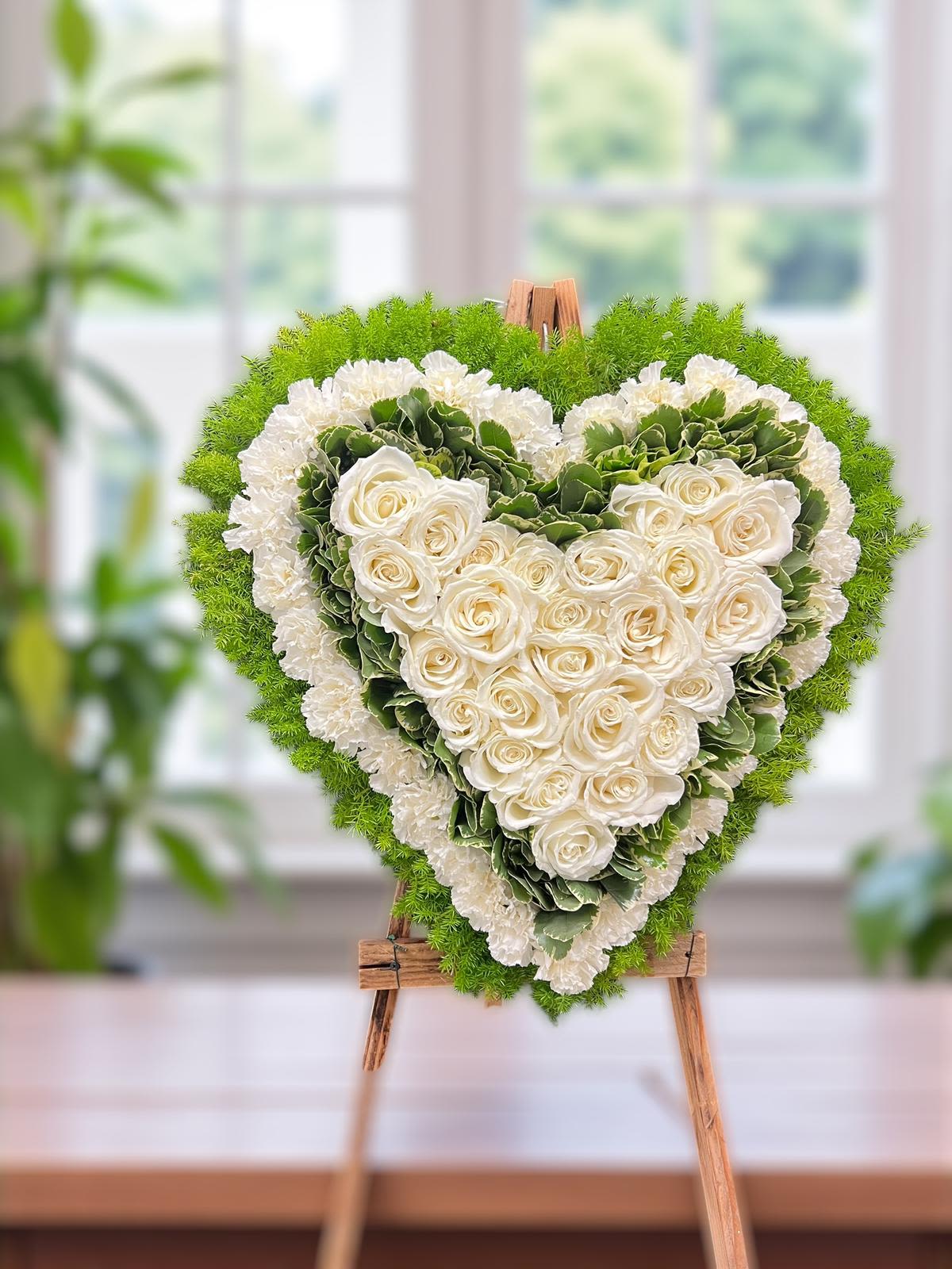 Heart-shaped floral arrangement of white roses and green hydrangeas on an easel