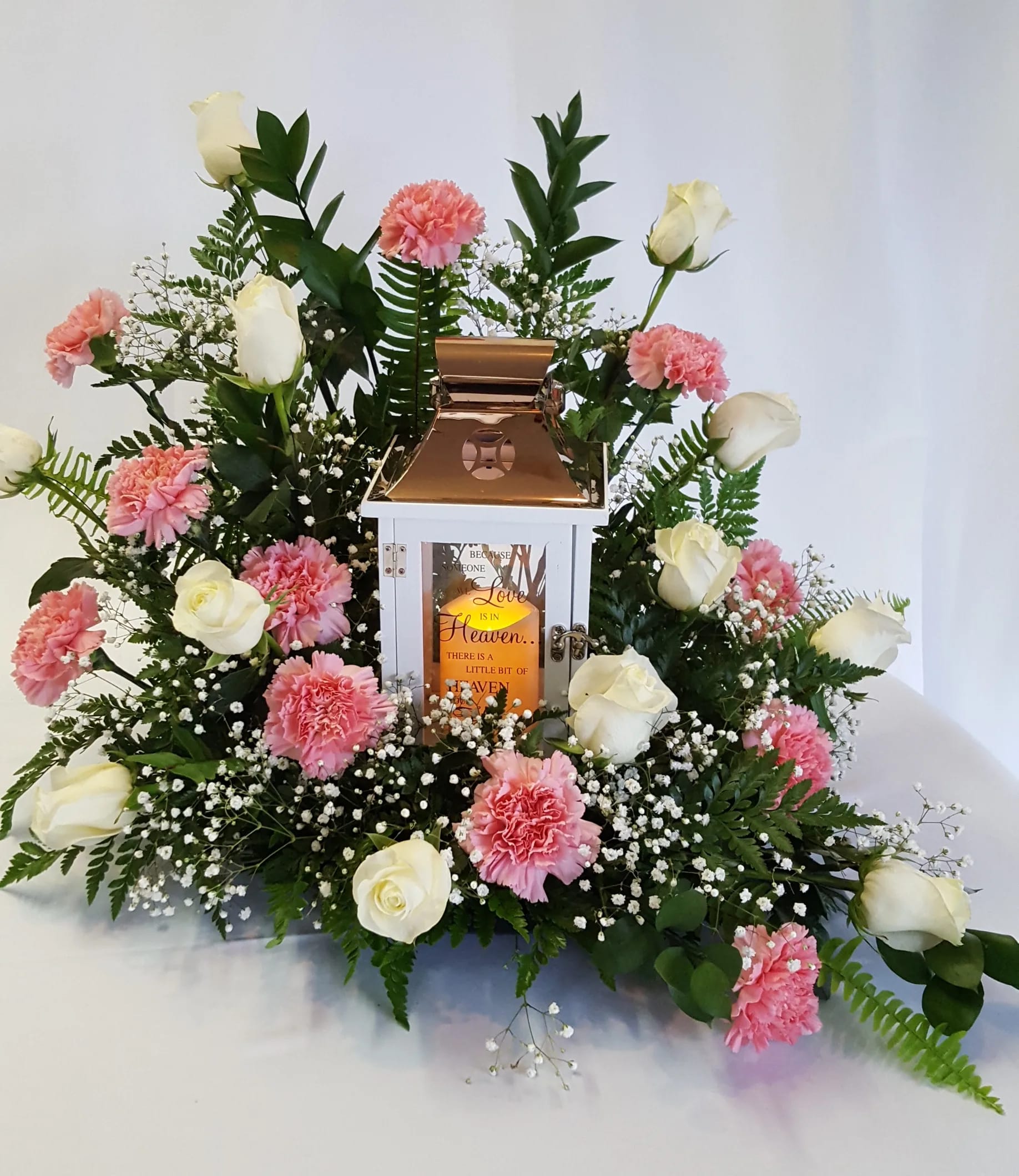 White roses and pink carnations arranged around a lantern centerpiece