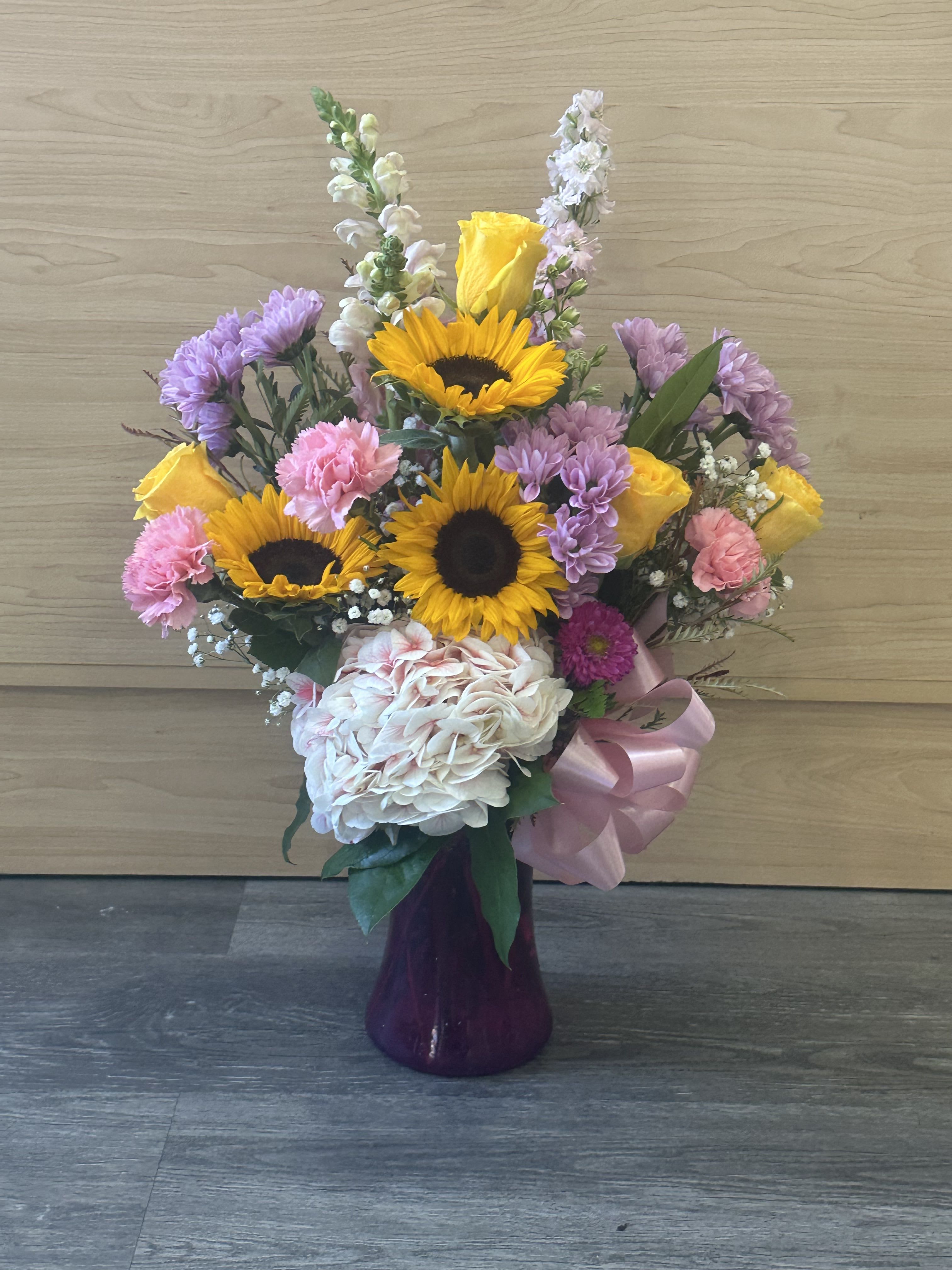 Mixed bouquet with sunflowers, roses, hydrangea, and carnations in a purple vase