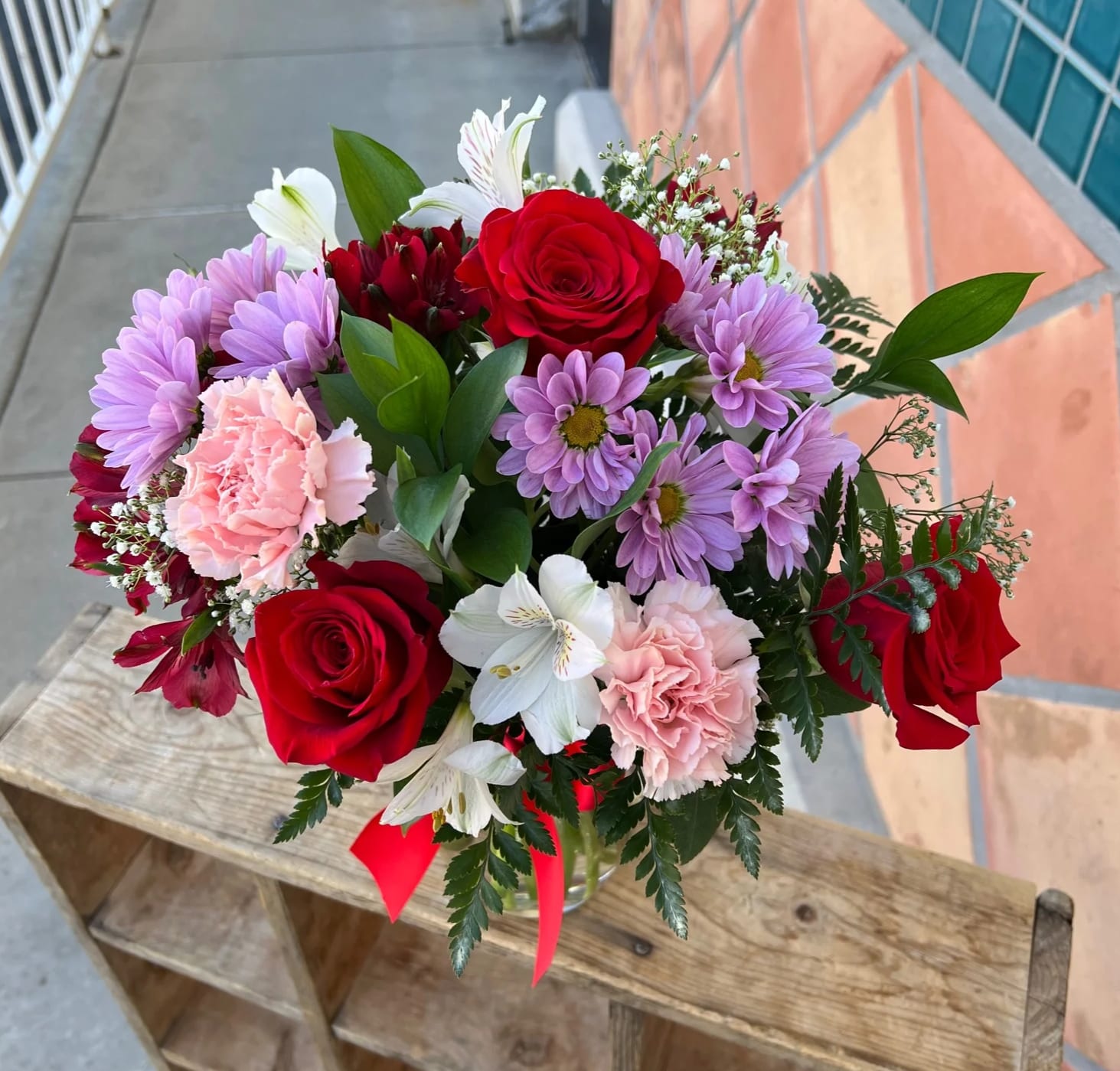 Bouquet of red roses, pink carnations, and purple daisies in a glass vase