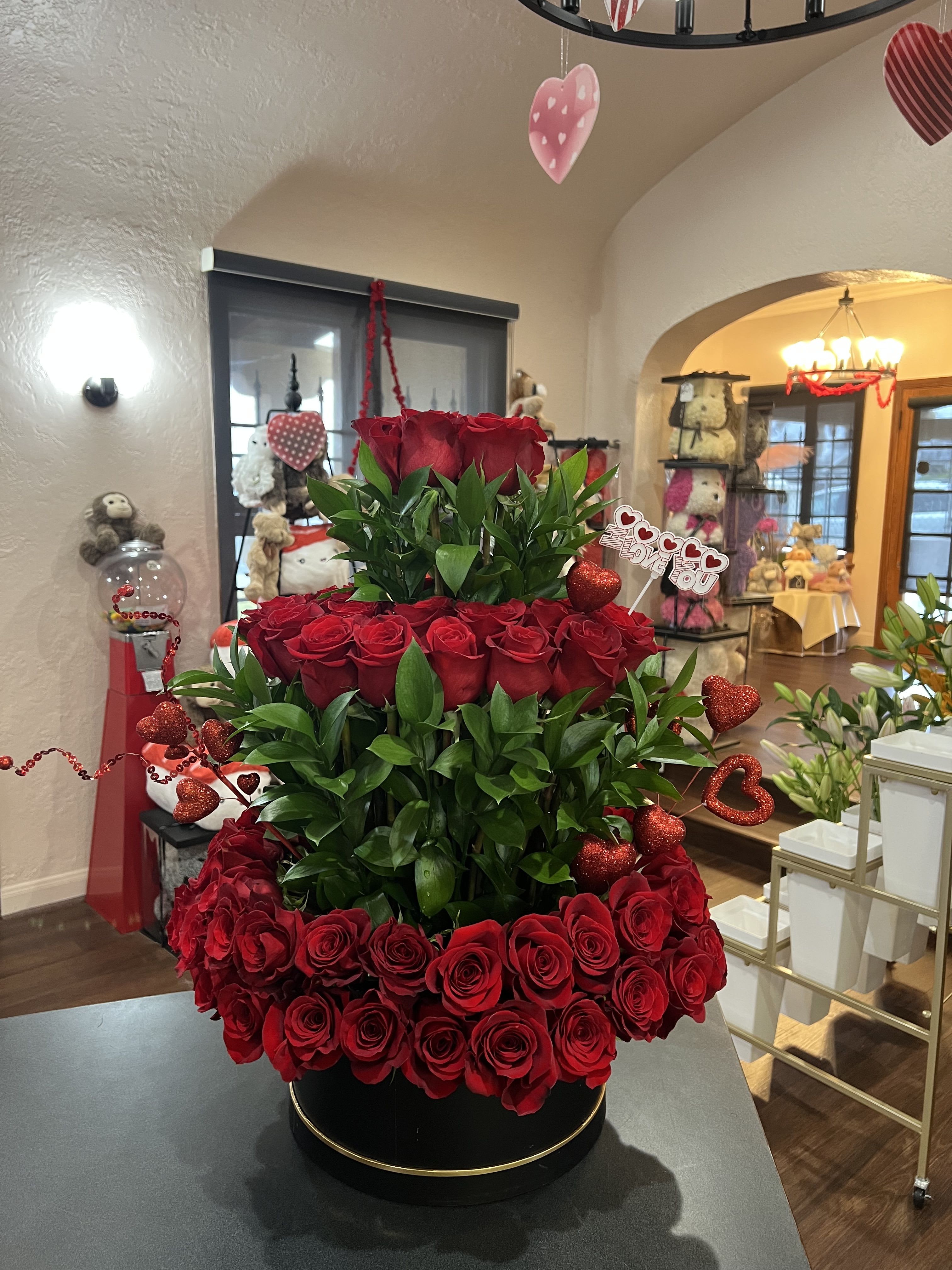 Tiered arrangement of red roses with heart decorations in a black round box