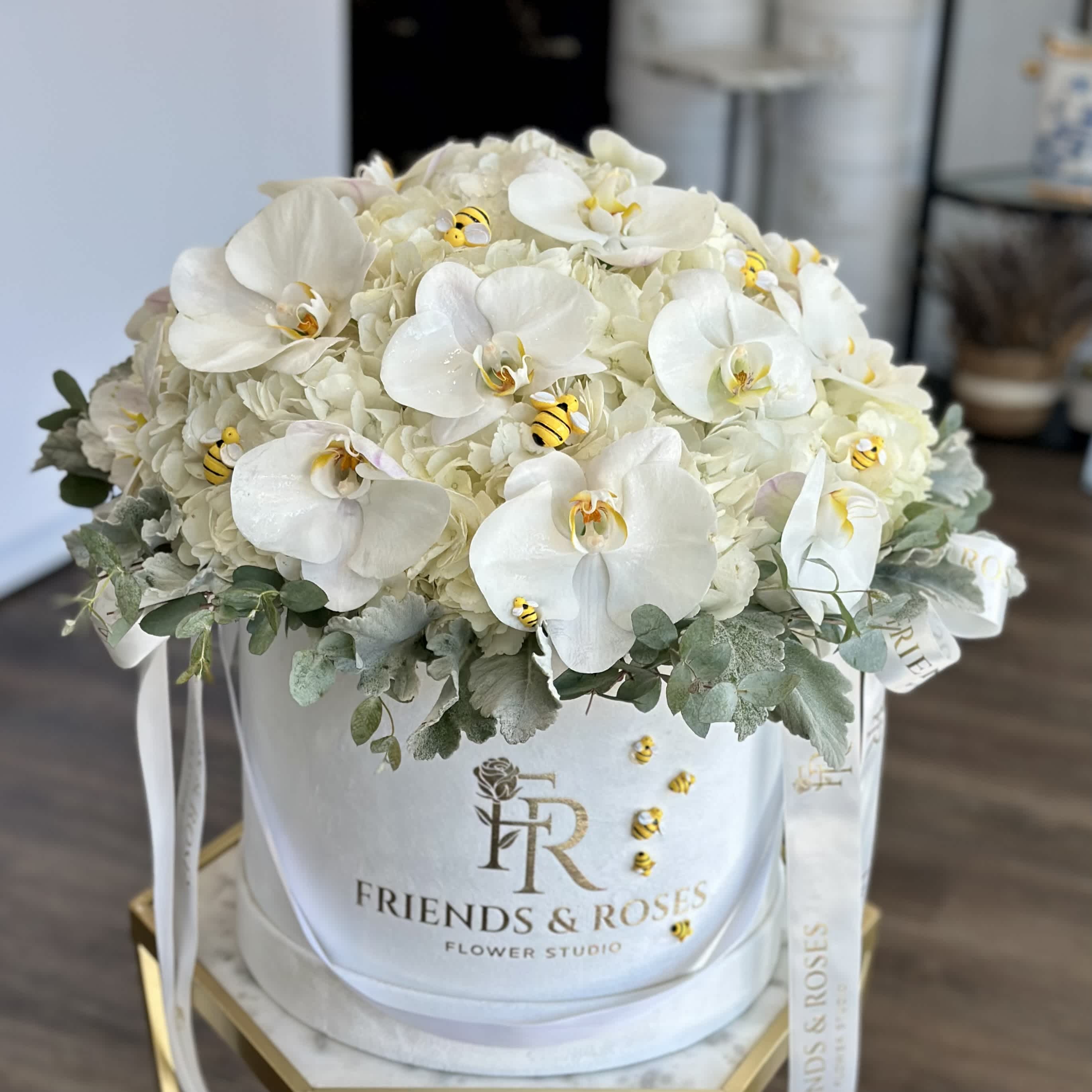 White orchids and hydrangeas in a round hatbox with ribbon