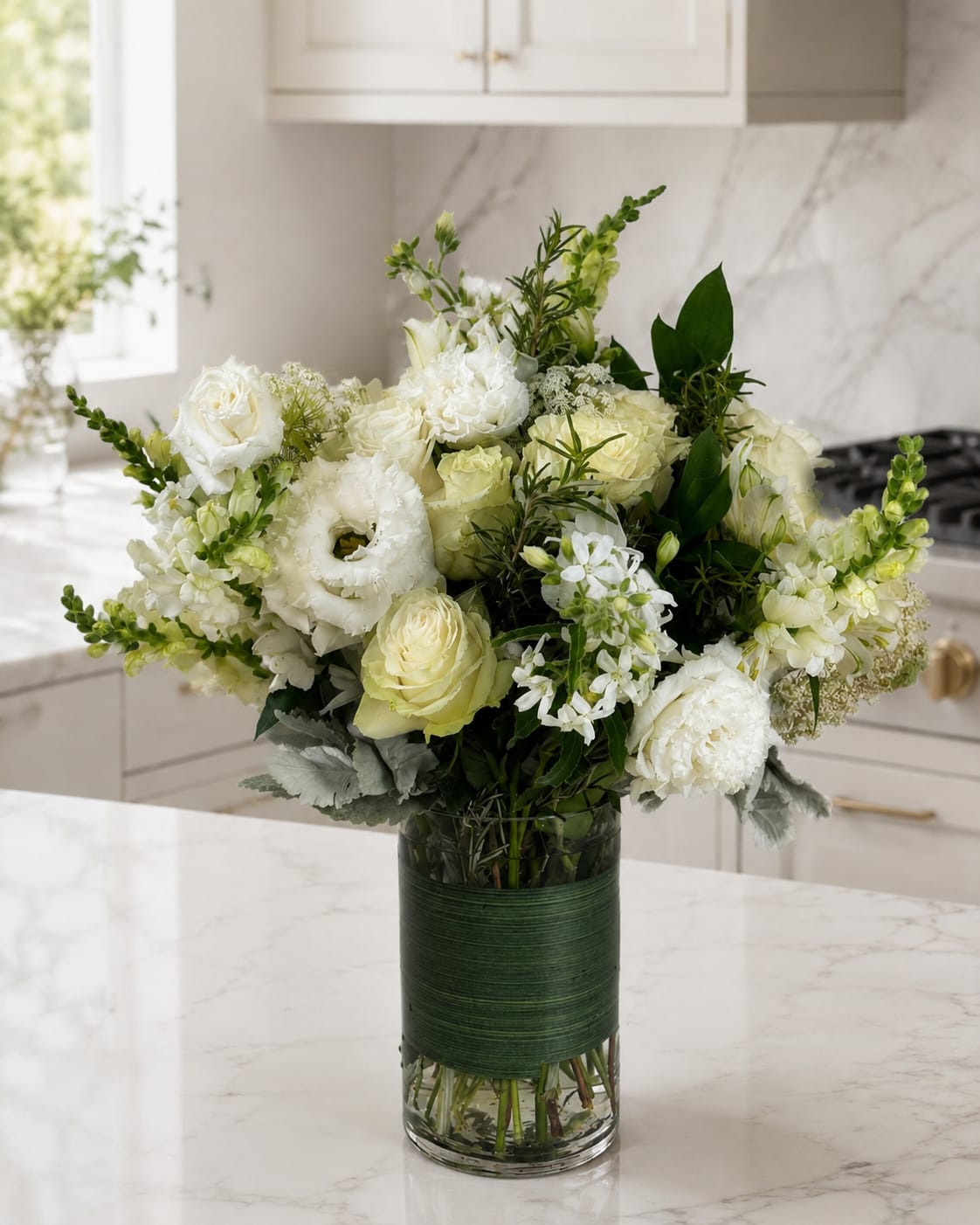 White floral arrangement in a glass vase with green accents