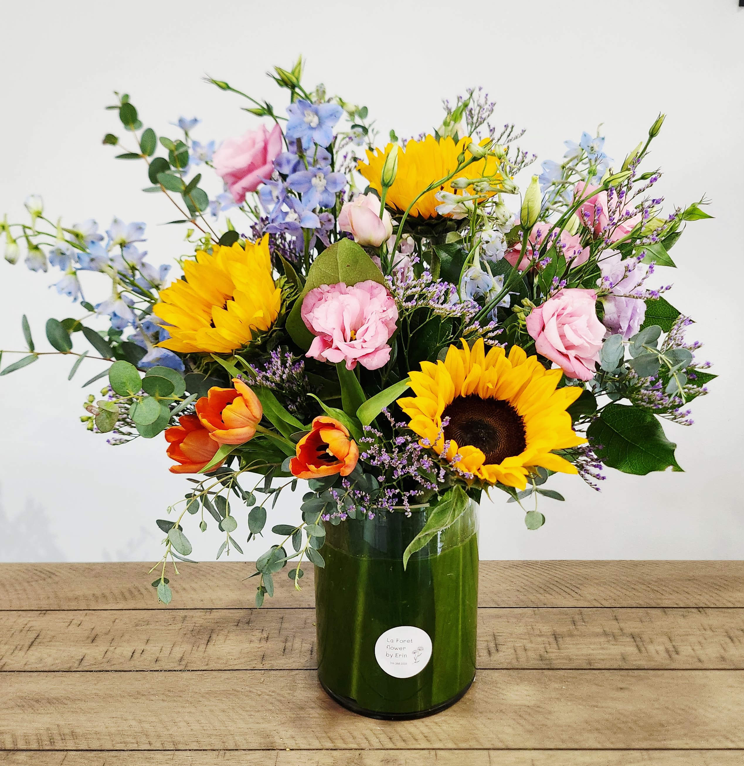 Mixed bouquet with sunflowers, pink blooms, and blue flowers in a green vase