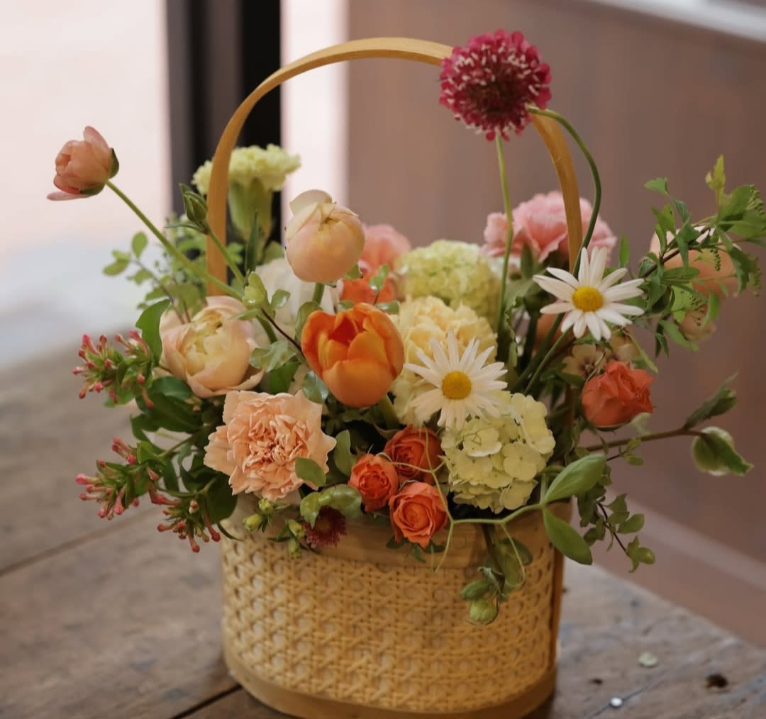 Basket arrangement with orange, peach, pink, and white flowers