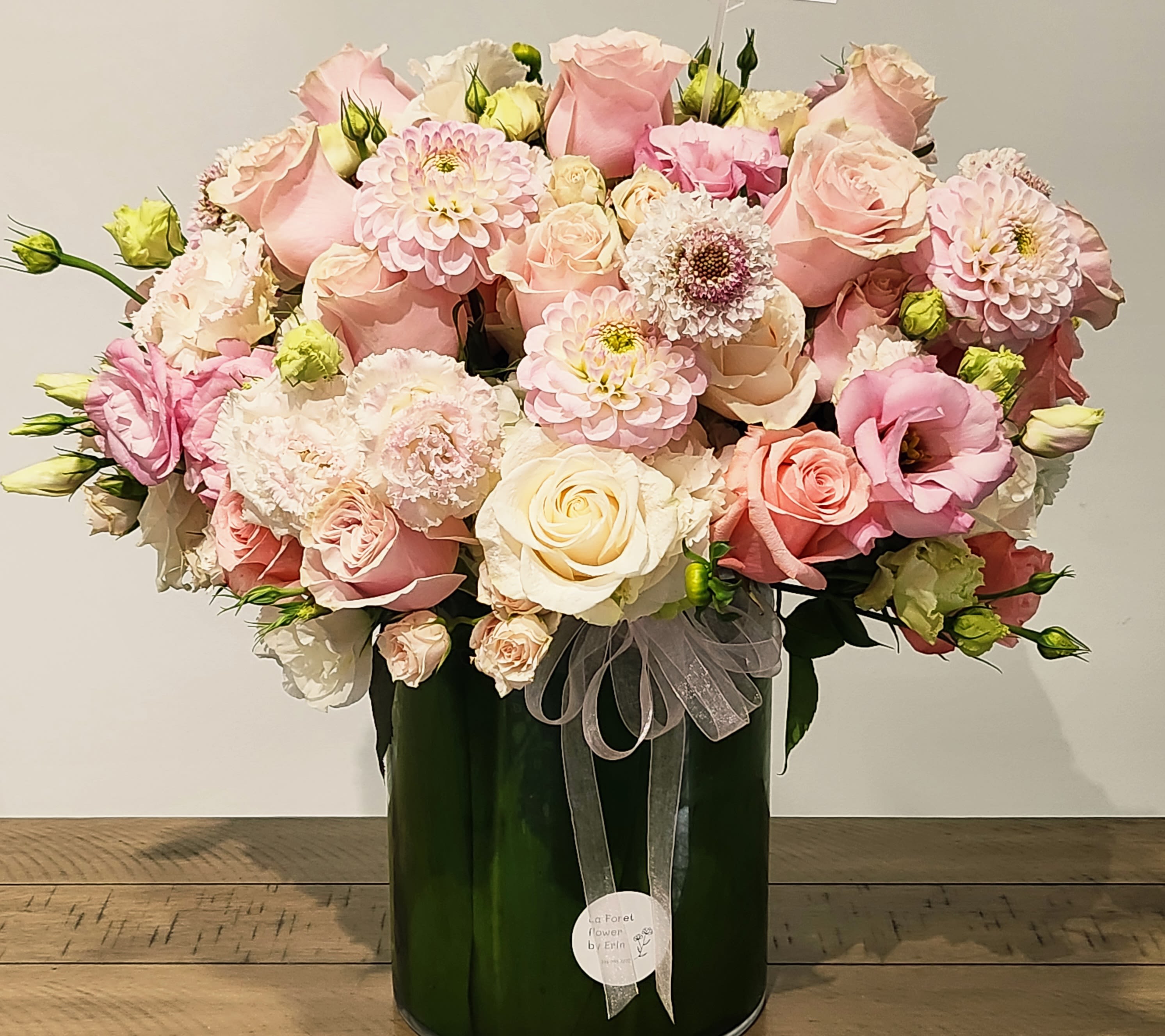 Pink and cream rose bouquet in a dark green vase with a sheer ribbon
