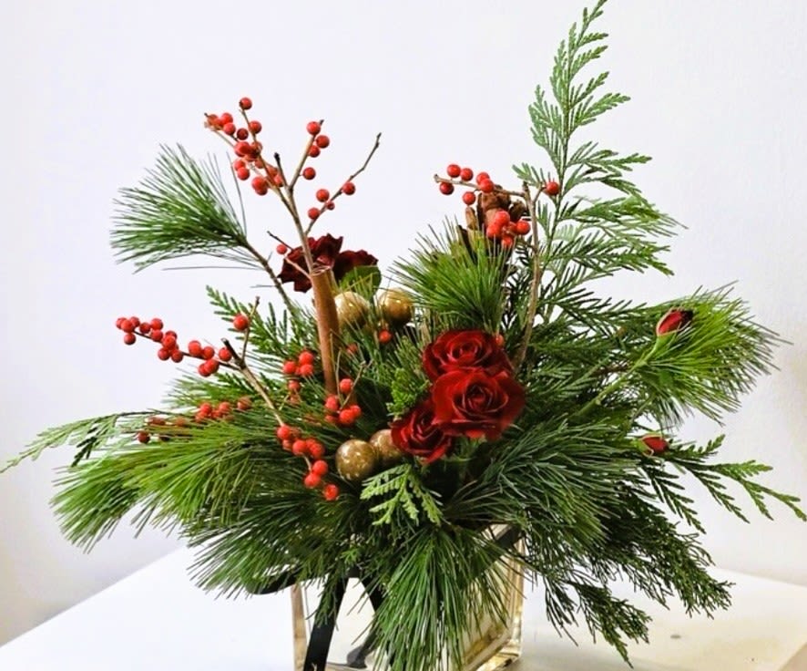 Holiday arrangement with red roses, pine, and red berries in a vase