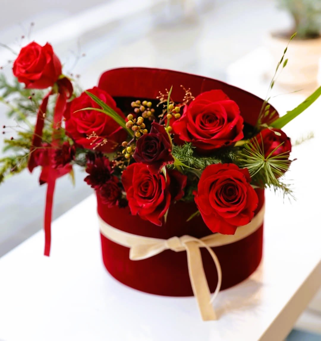 Red roses arranged in a burgundy hat box with a cream ribbon