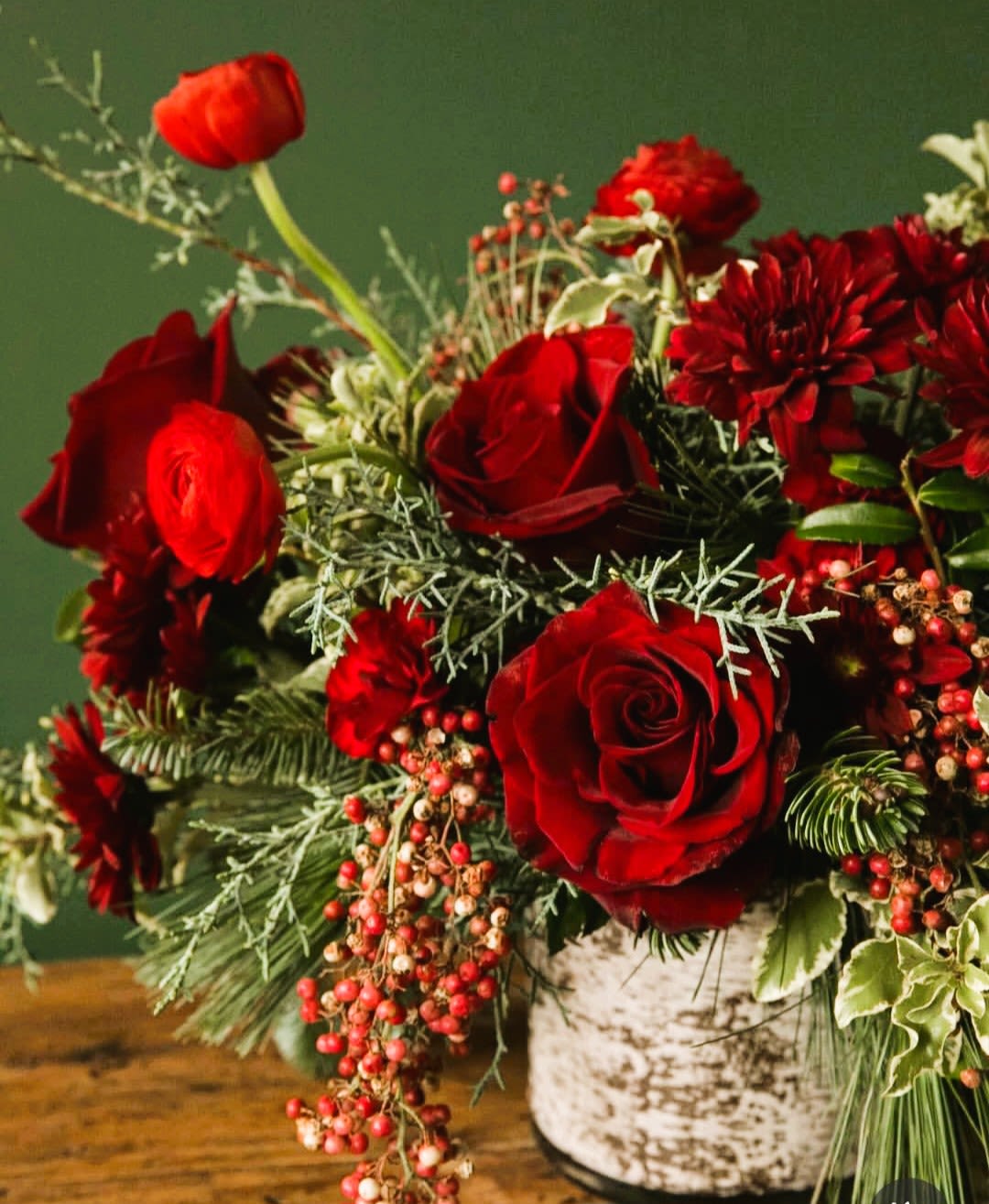 Red roses and red blooms in a white vase with berries and greenery