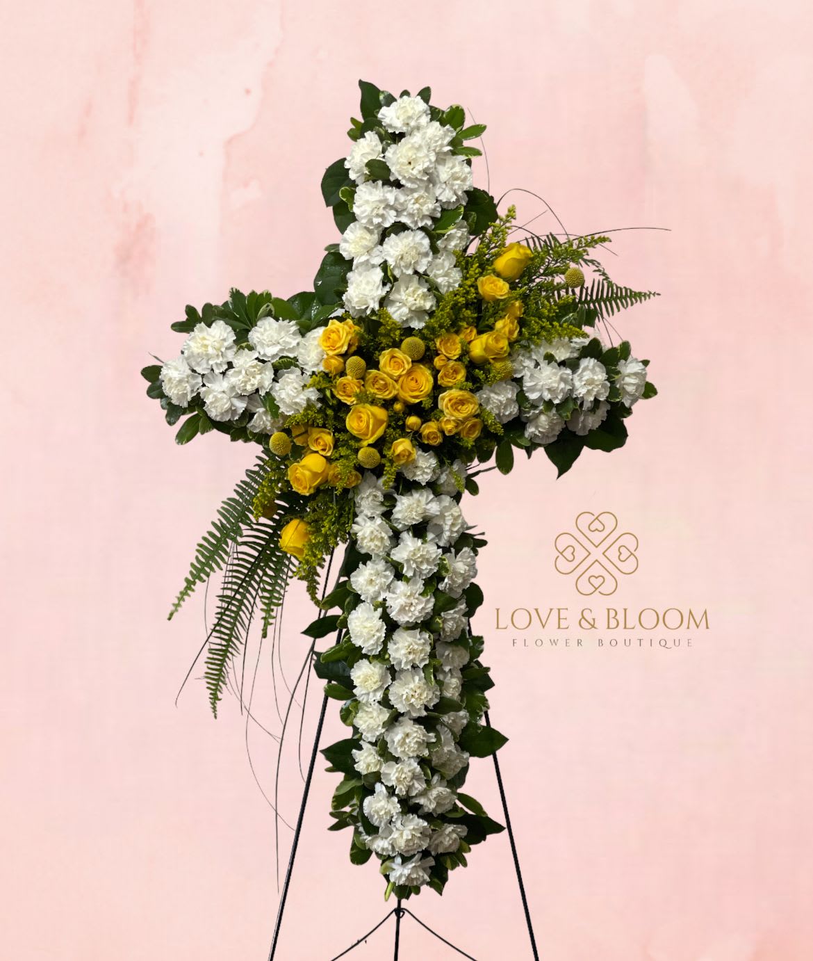 Cross-shaped floral tribute with white and yellow flowers on a stand