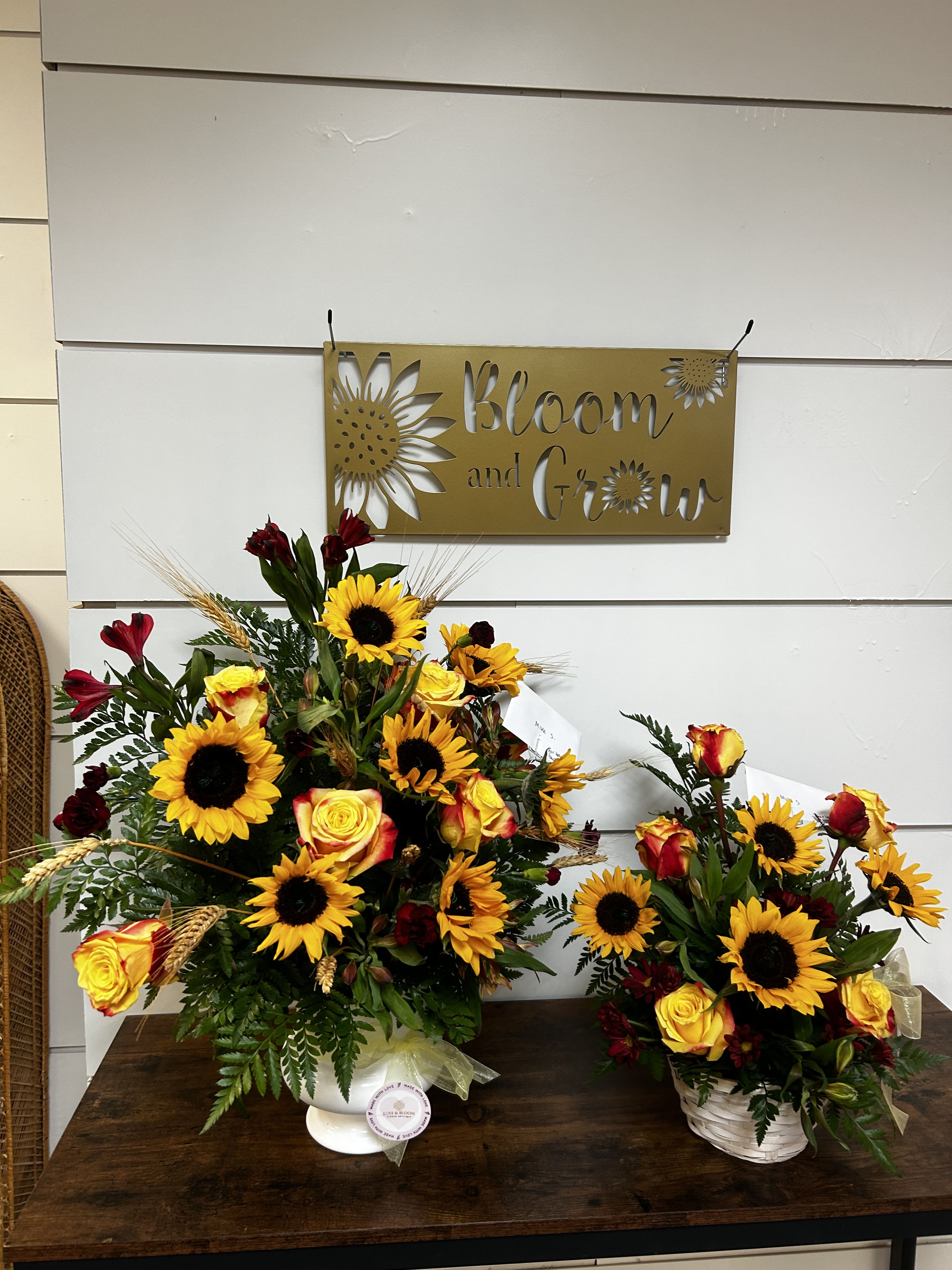 Two sunflower and rose arrangements in white containers on a table
