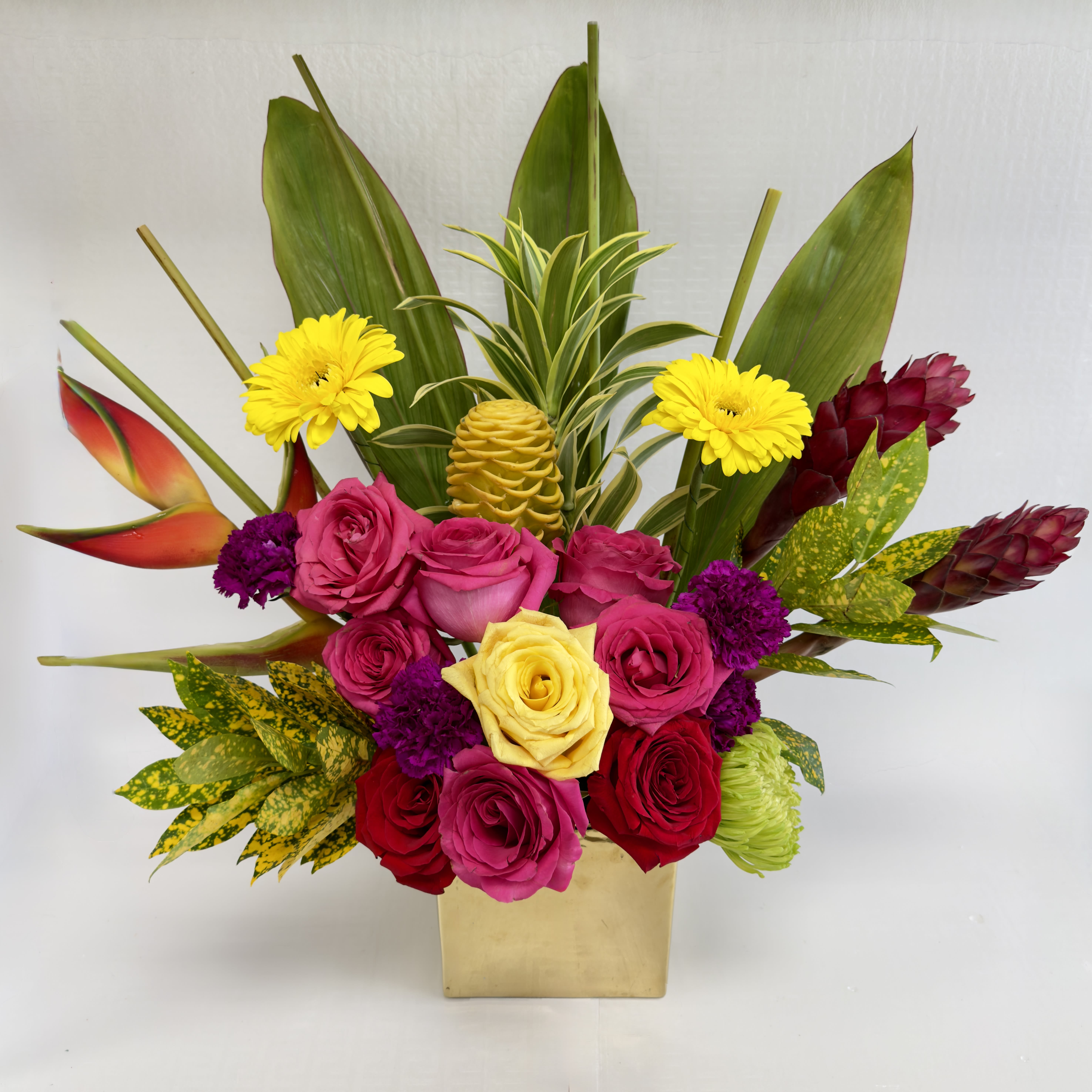 Bright mixed bouquet in a gold vase with roses and tropical blooms