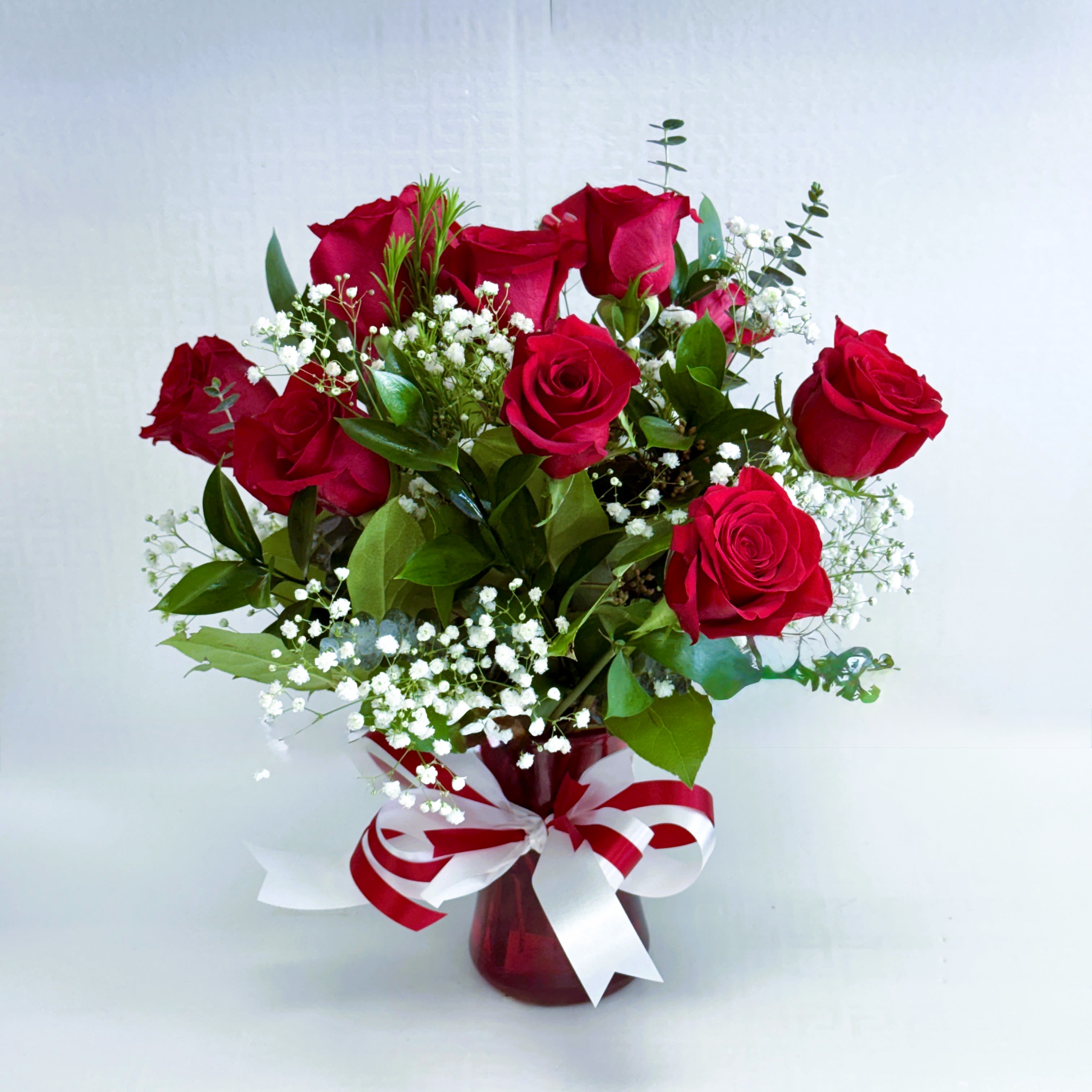 Crimson Grace Bouquet - A classic and elegant arrangement of rich red roses accented with delicate white baby’s breath and lush greenery, beautifully presented in a red glass vase with a coordinating ribbon. Perfect for expressing love, romance, or heartfelt appreciation on any special occasion.