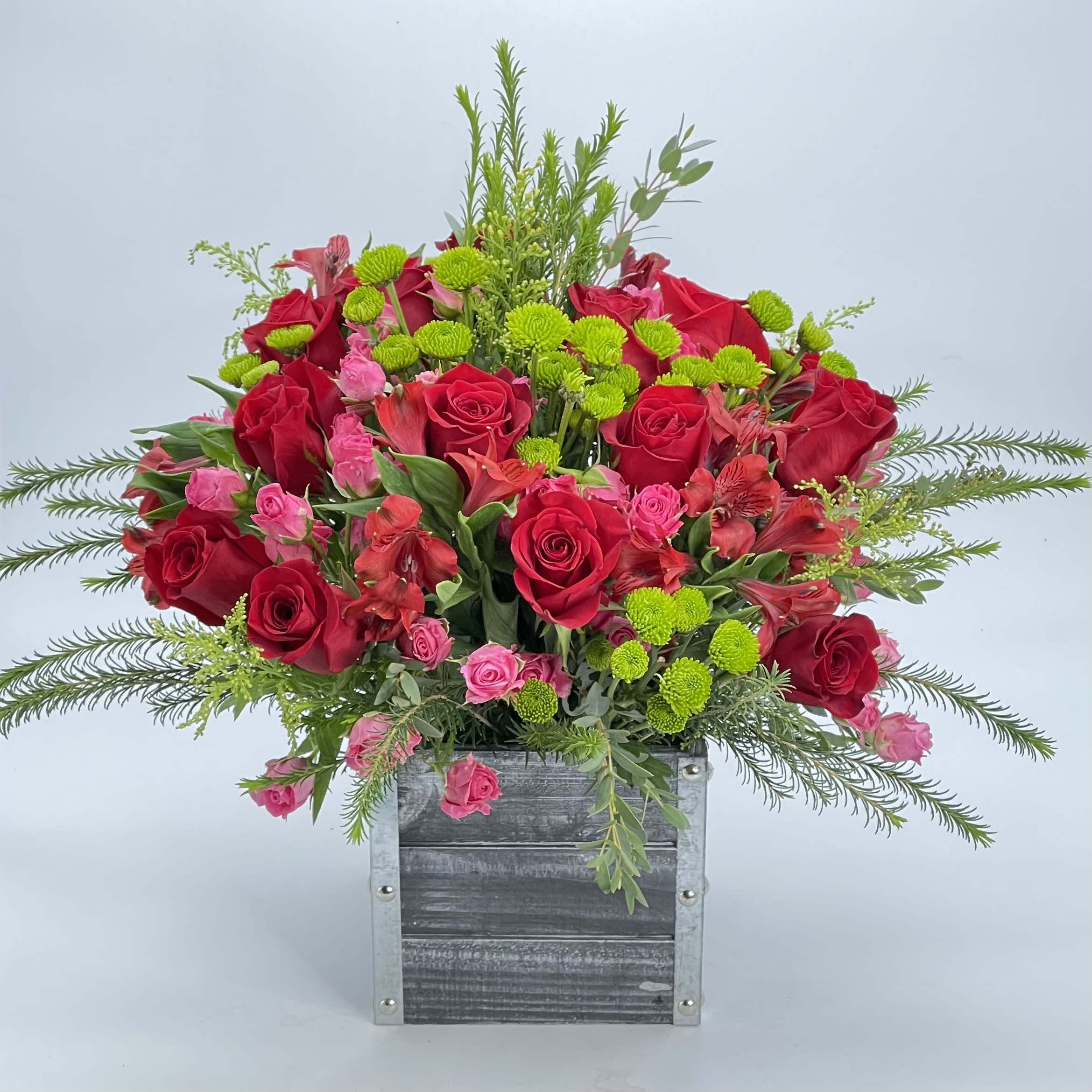 Arrangement of red roses, pink spray roses, and green button mums in a rustic square box.