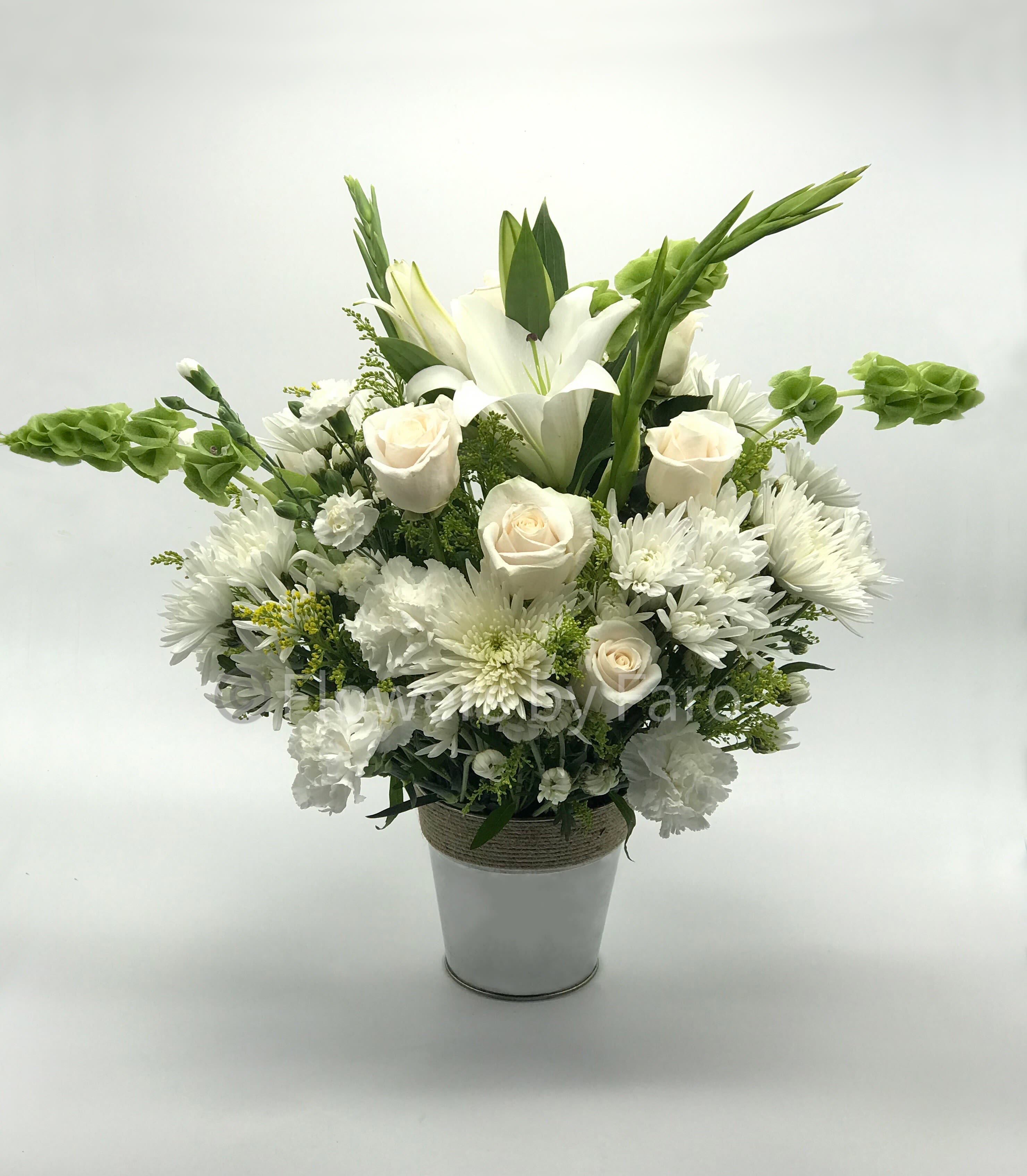 White and cream roses, lilies, and mums with green bells of Ireland in a white metal pot
