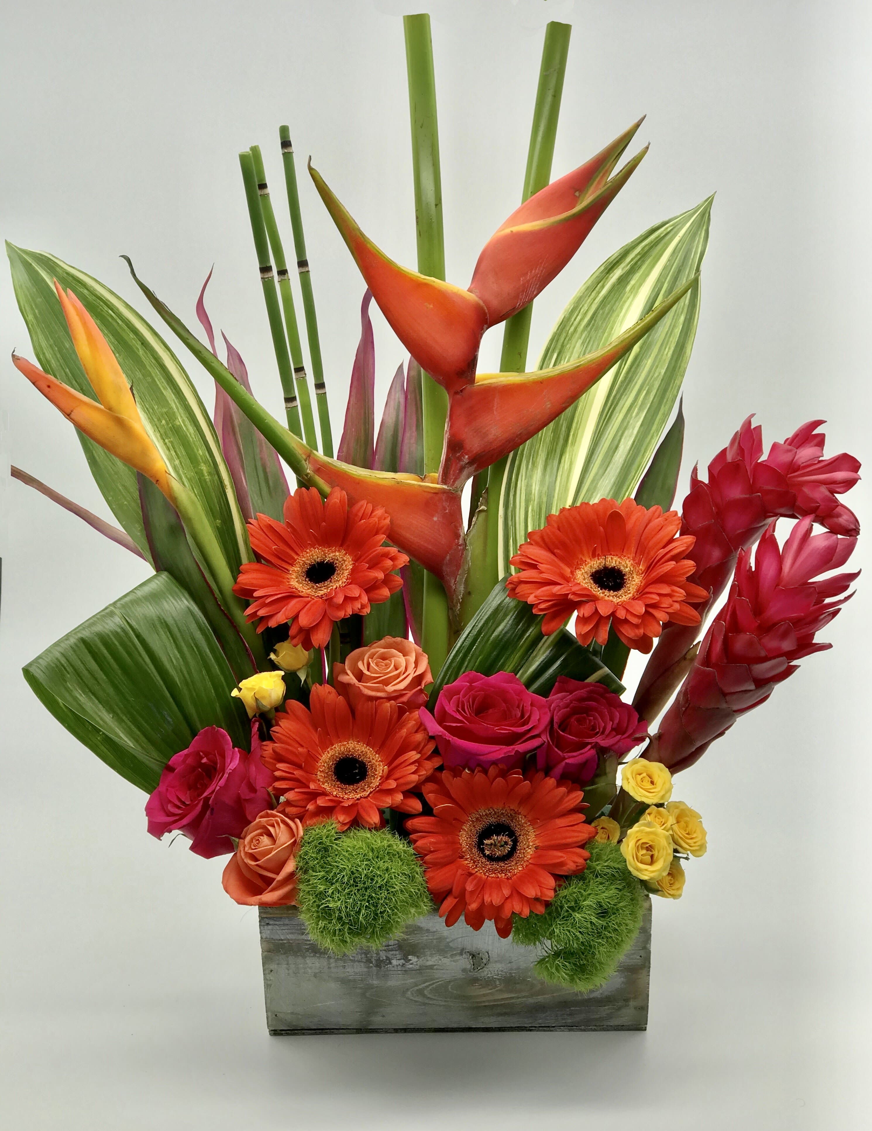 Tall tropical arrangement with orange gerberas, roses, and exotic blooms in a wooden box
