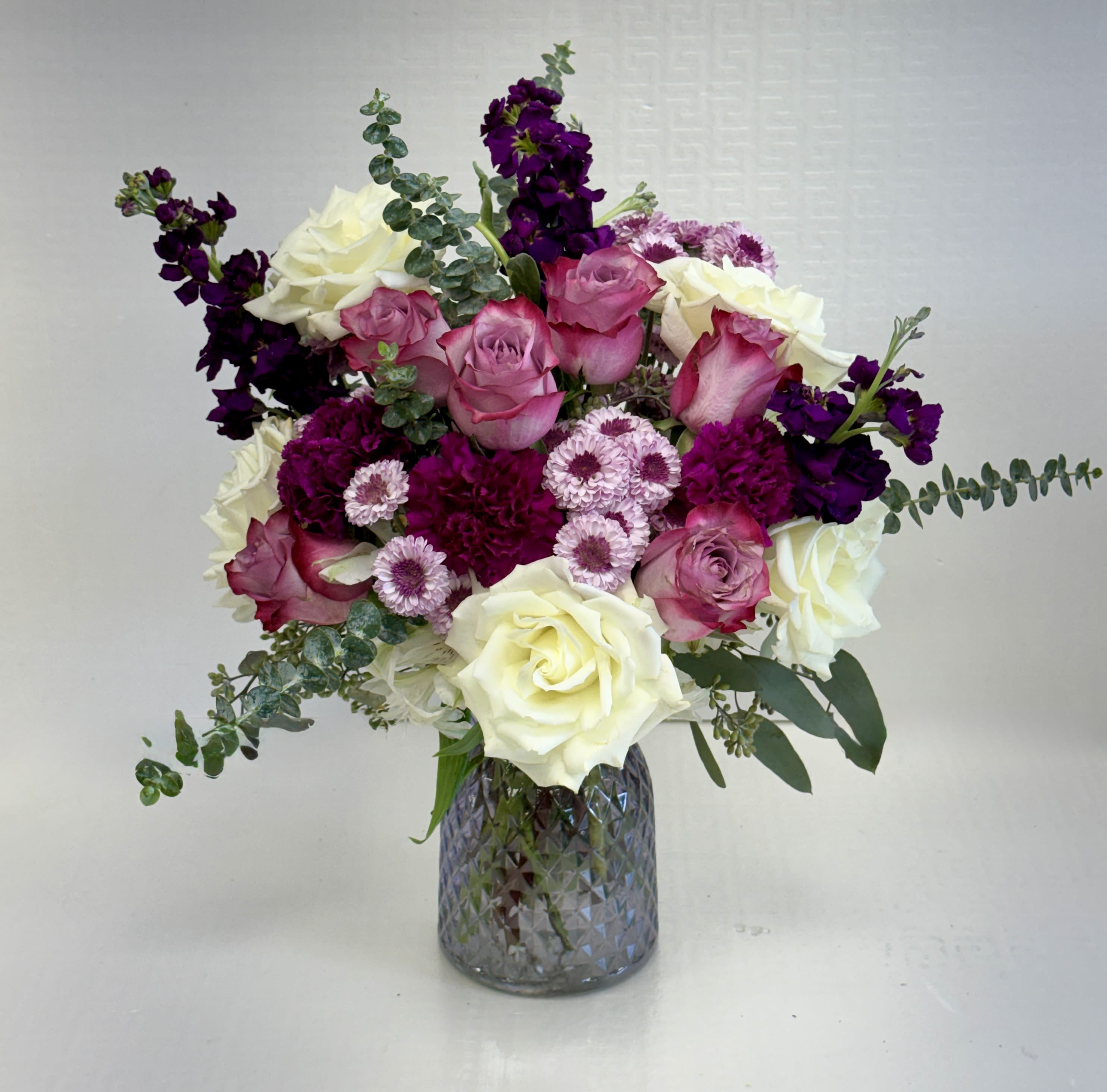 Mixed bouquet of white roses, pink roses, and purple flowers in a gray textured glass vase