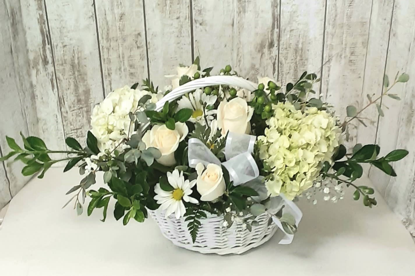 White roses and hydrangeas in a white basket with a ribbon