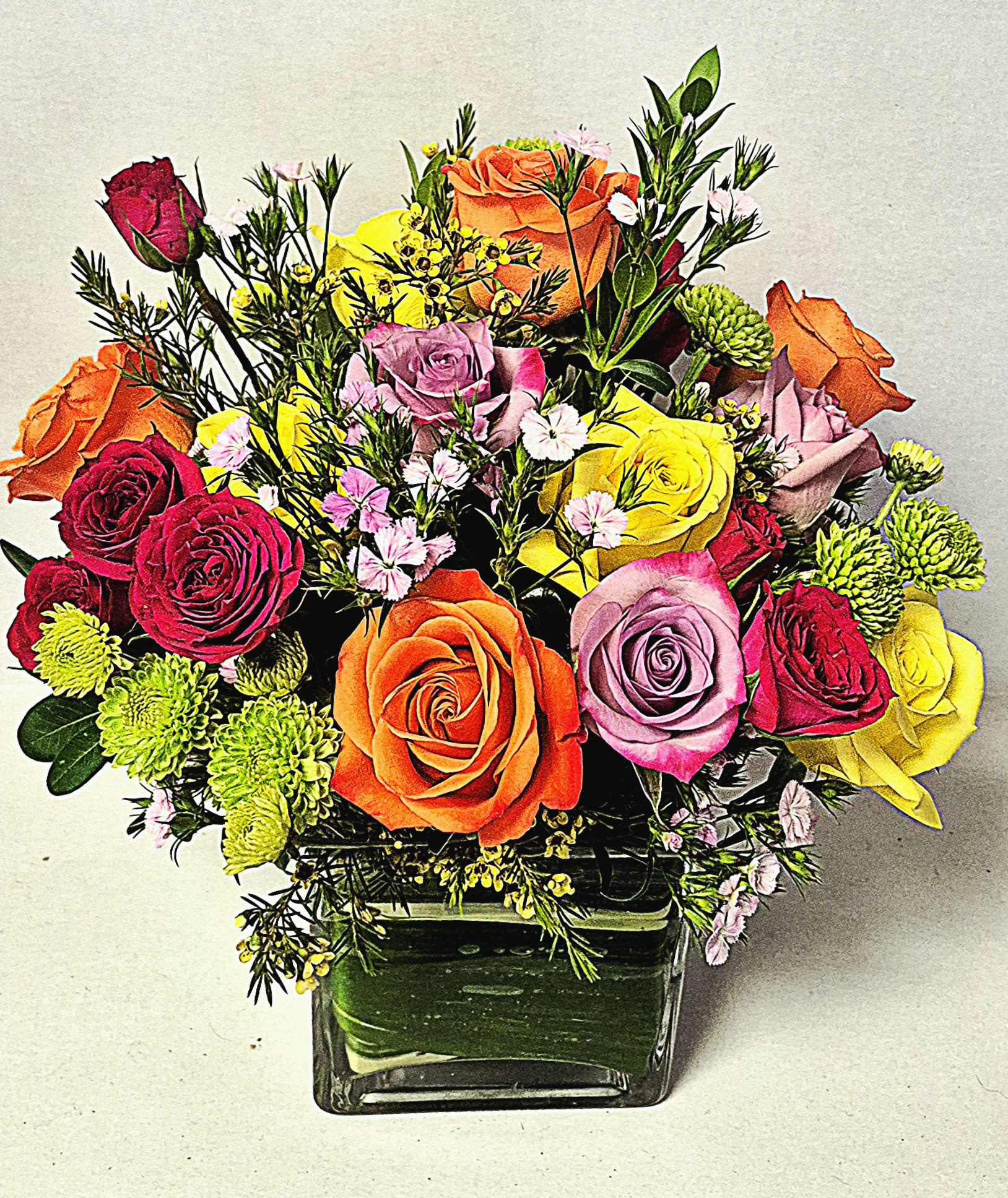 Rainbows and Roses - A Beautiful assortment of roses and spray roses combined with colorful fillers in a clear modern cube with a green leaf like ribbon lining. The perfect arrangement for most gift giving occasions!