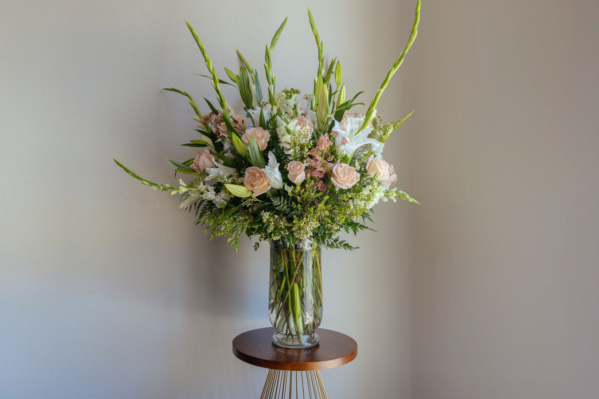 Tall bouquet of pale roses, white lilies, and greenery in a clear glass vase