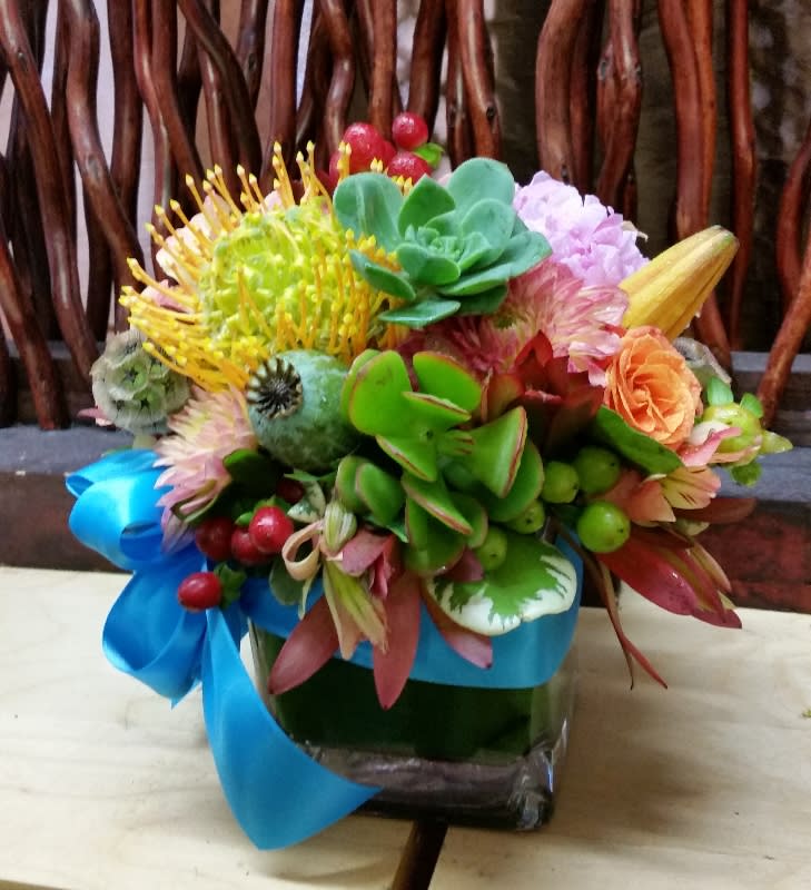 Colorful bouquet with succulents and mixed flowers in a glass vase tied with blue ribbon