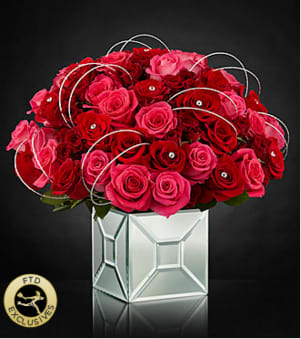 Blushing Extravagance™ Luxury Bouquet - Designed to capture the heart, this bouquet goes above and beyond to create a space where modern style and love's every wish unite. Hot pink roses, red roses, and red spray roses are arranged to perfection and embellished with sparkling stone accents at the center of select blooms, as well as, silver wires to create a fascinating looping effect, taking the average rose bouquet to a new level of sophistication. Tying everything together is the modern mirrored vase that brings light and love to this unique design. IMPRESSIVE bouquet includes 41 stems with vase. Approx. 15"H x 15"W. STUNNING bouquet includes 53 stems with vase. Approx. 16"H x 16"W.  Your purchase includes a complimentary personalized gift message.