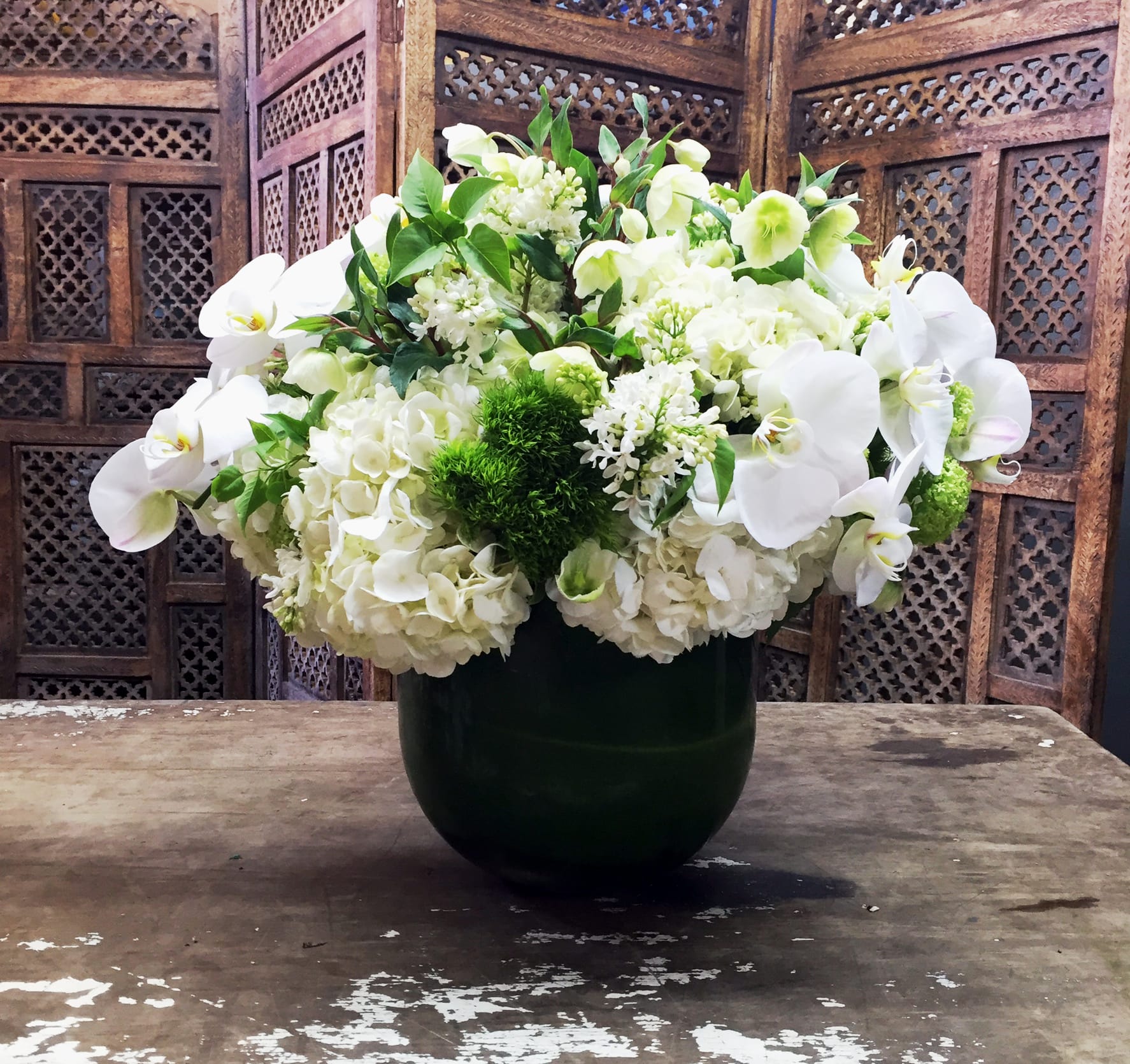 White floral arrangement in a dark vase with orchids and hydrangeas