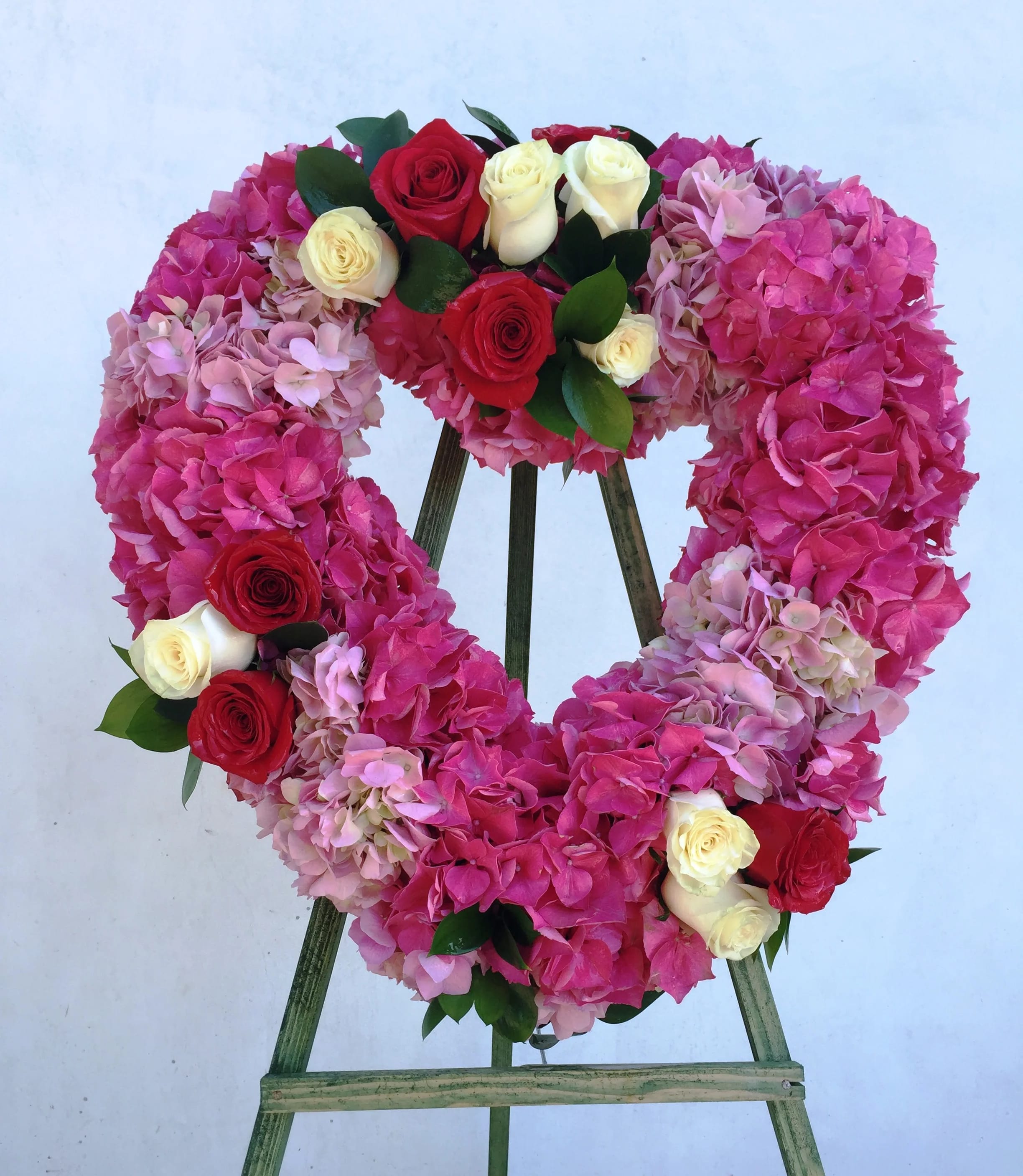Heart-shaped floral wreath of pink hydrangeas and red and white roses on a stand