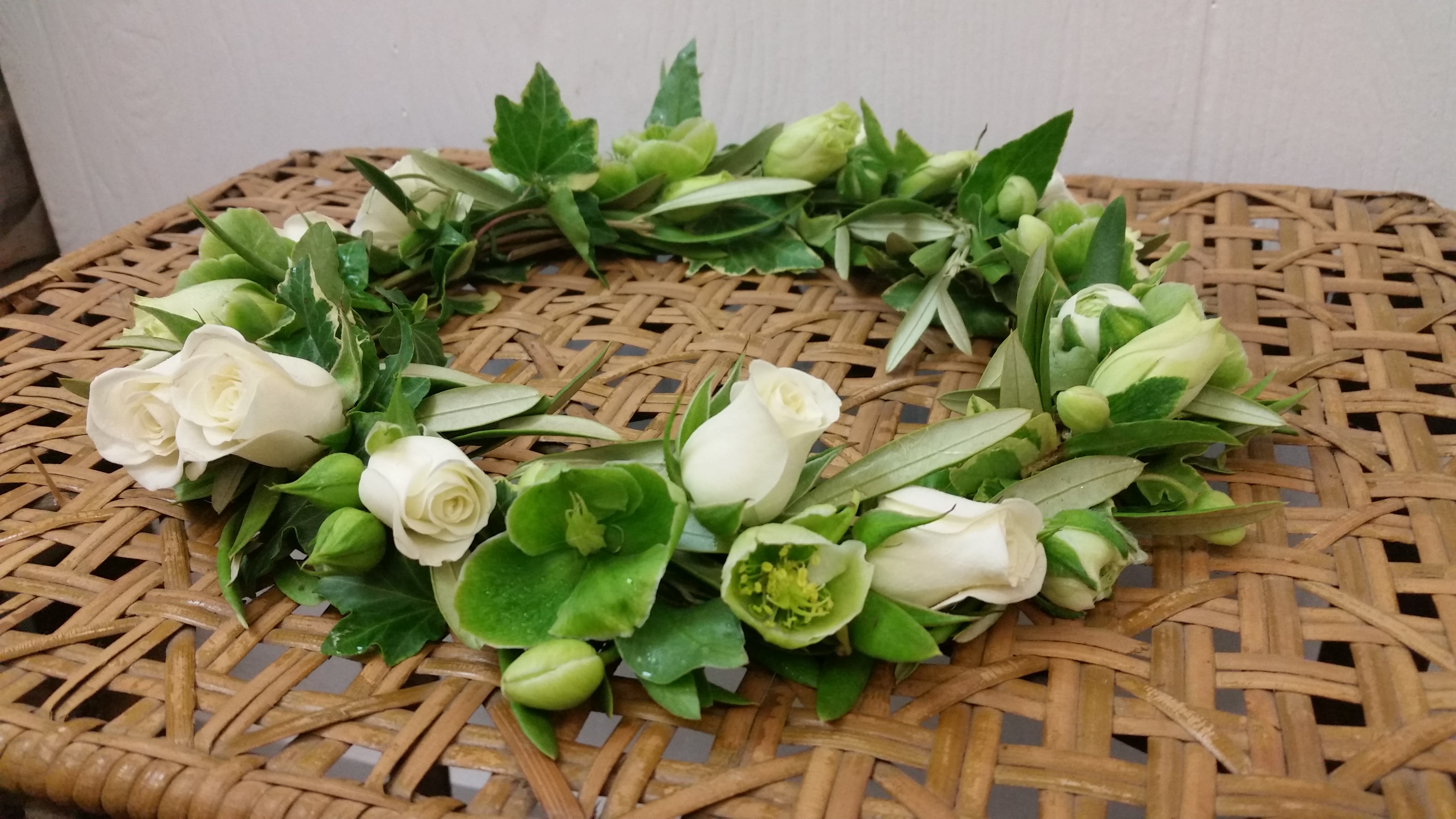 White rose and green flower crown on a woven surface