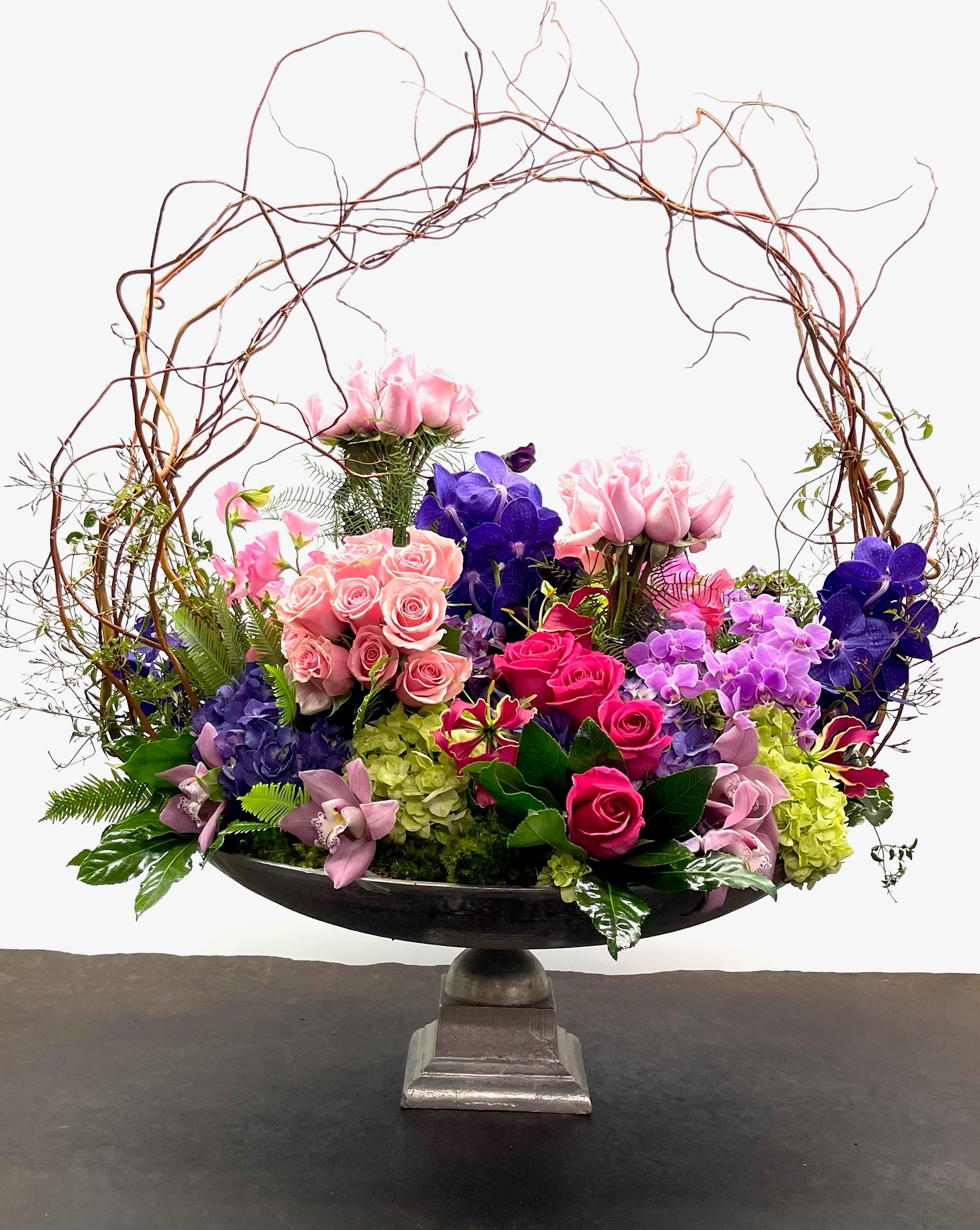 Large floral arrangement with pink, purple, and green blooms in a pedestal bowl