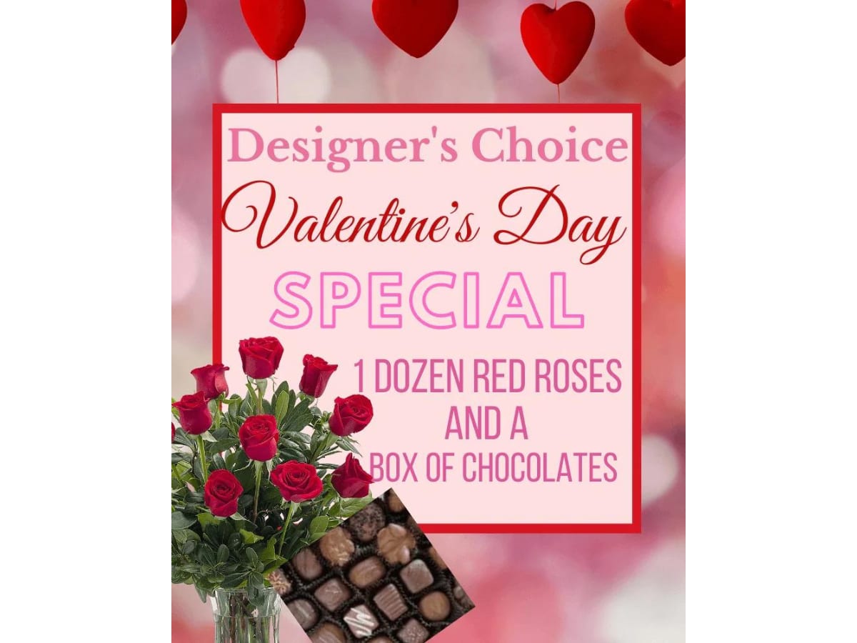 Red roses in a glass vase beside a box of chocolates and a Valentine’s Day sign.