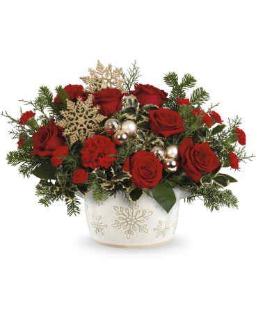 Red roses arranged in a white snowflake vase with holiday accents