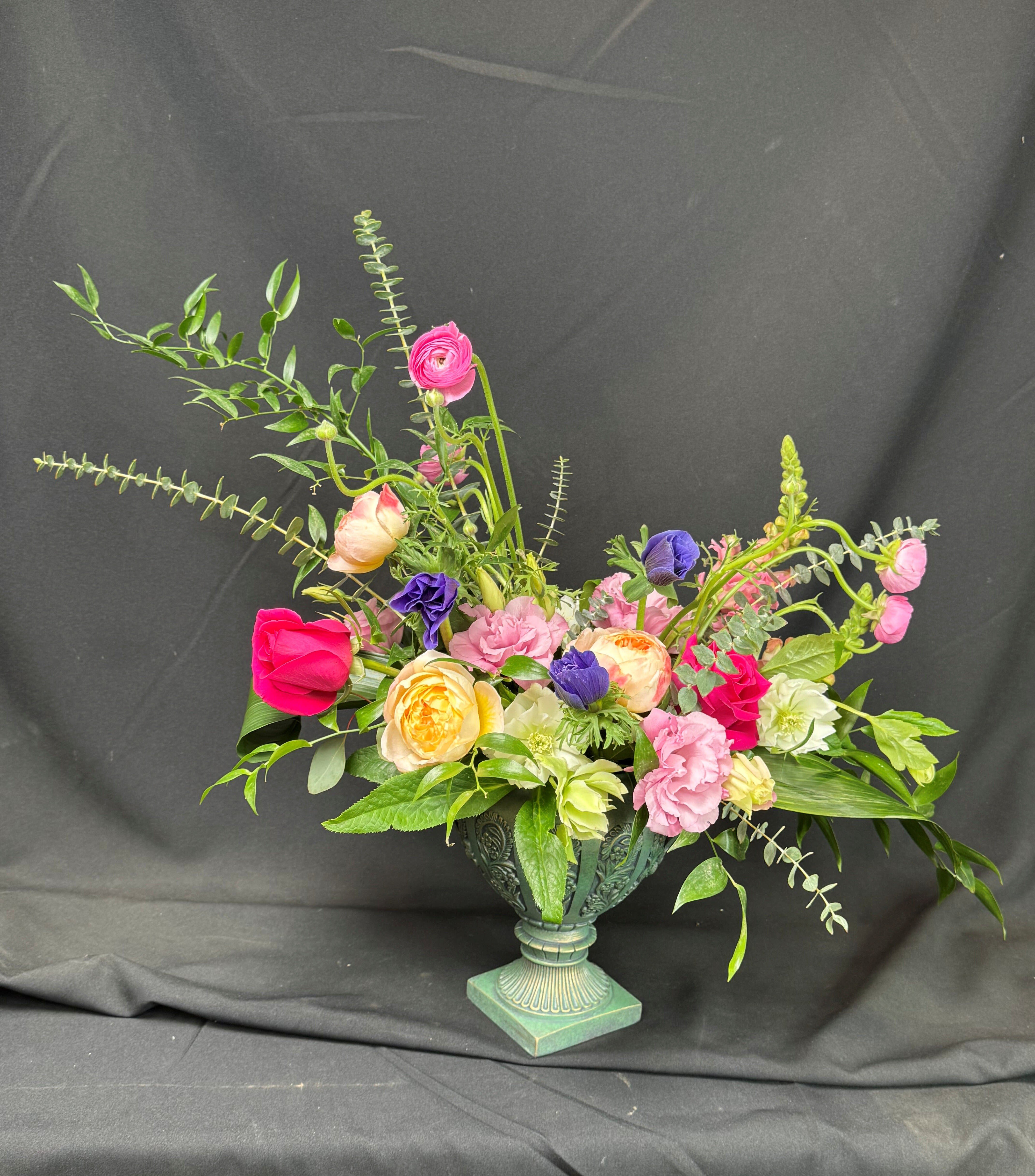 Mixed bouquet of pink, yellow, purple, and white flowers in a decorative urn vase