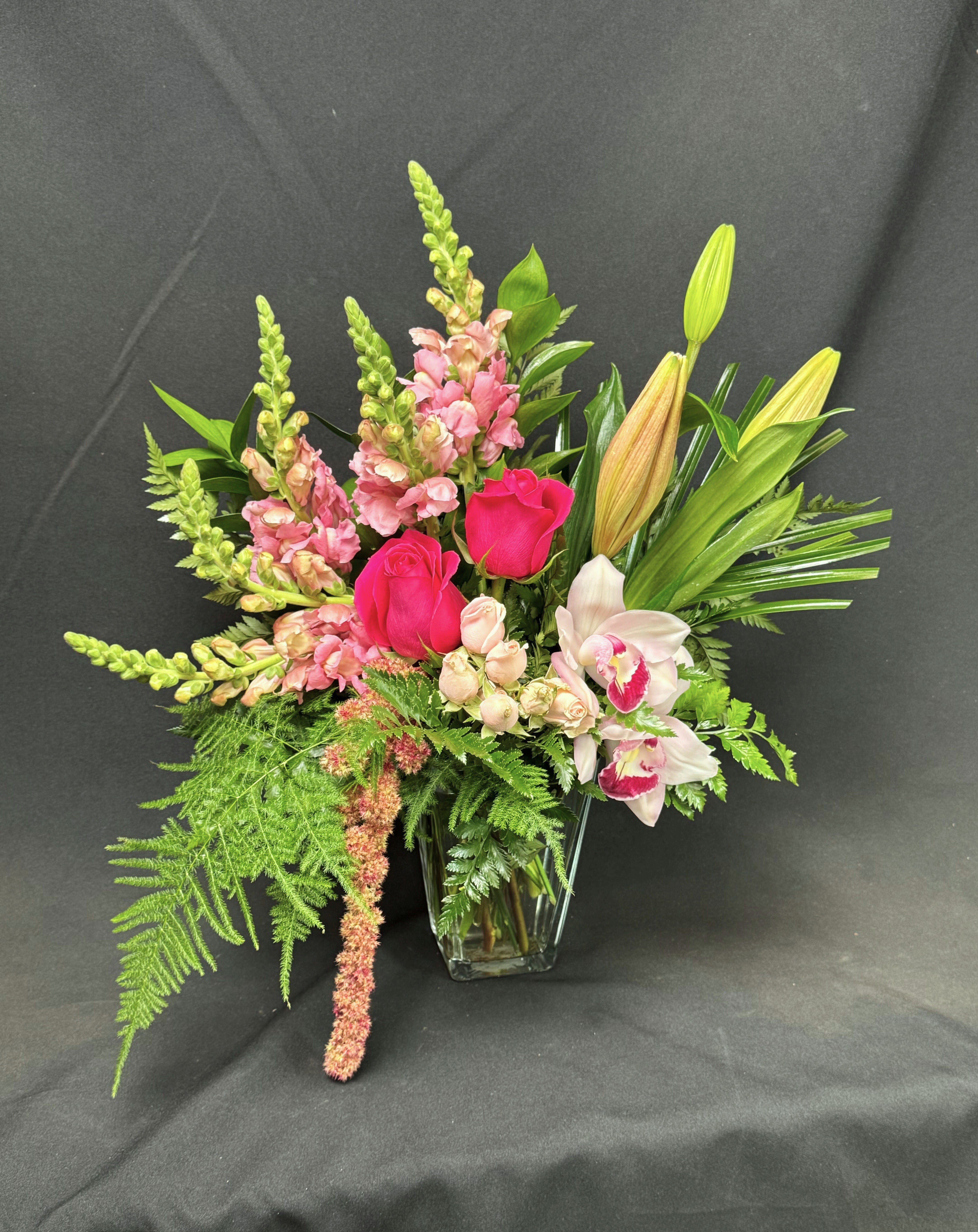 Pink roses and orchids in a clear glass vase with tall greenery