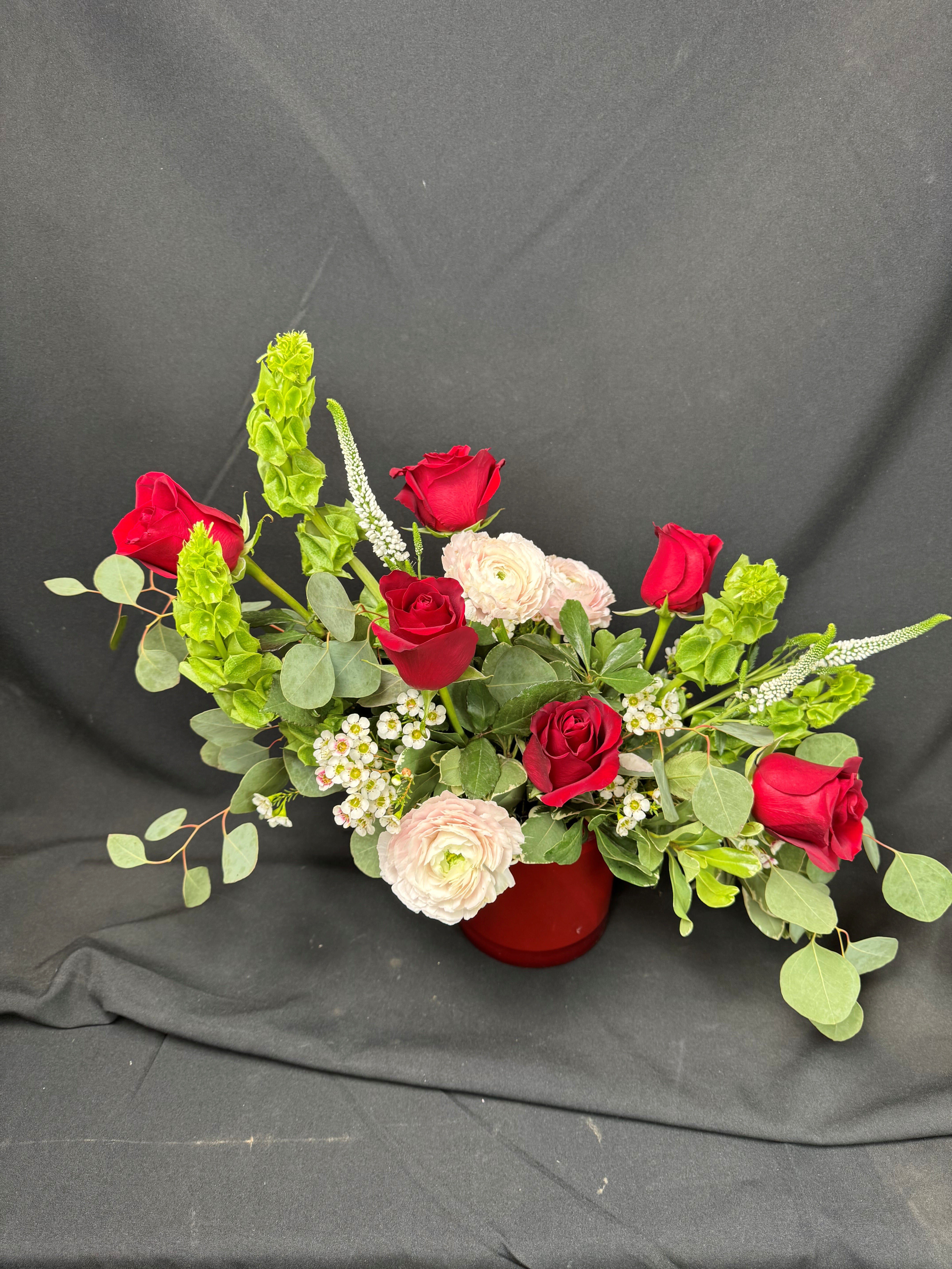 Red roses and pale ranunculus arranged in a red vase