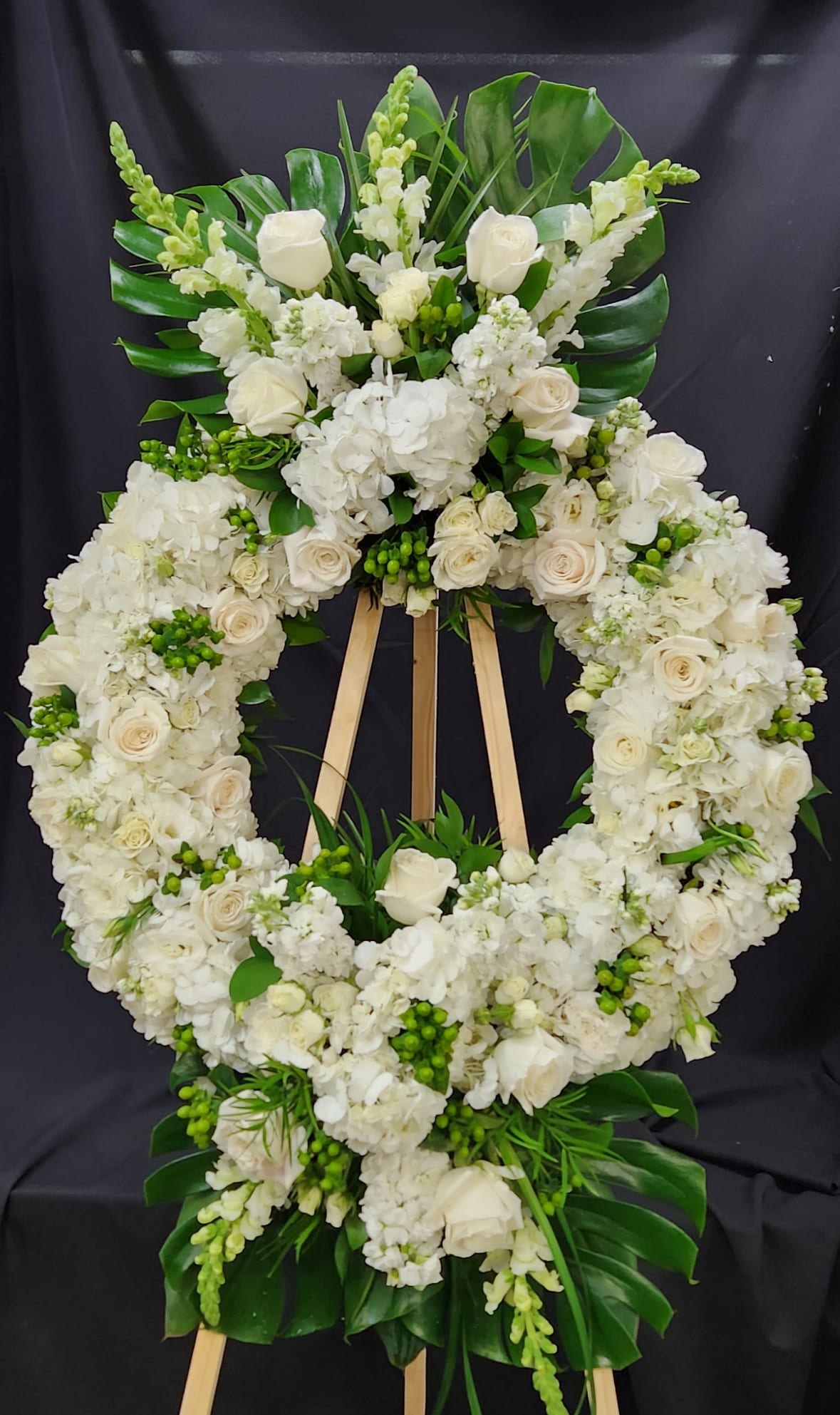 White floral funeral wreath on a wooden easel with roses and hydrangeas
