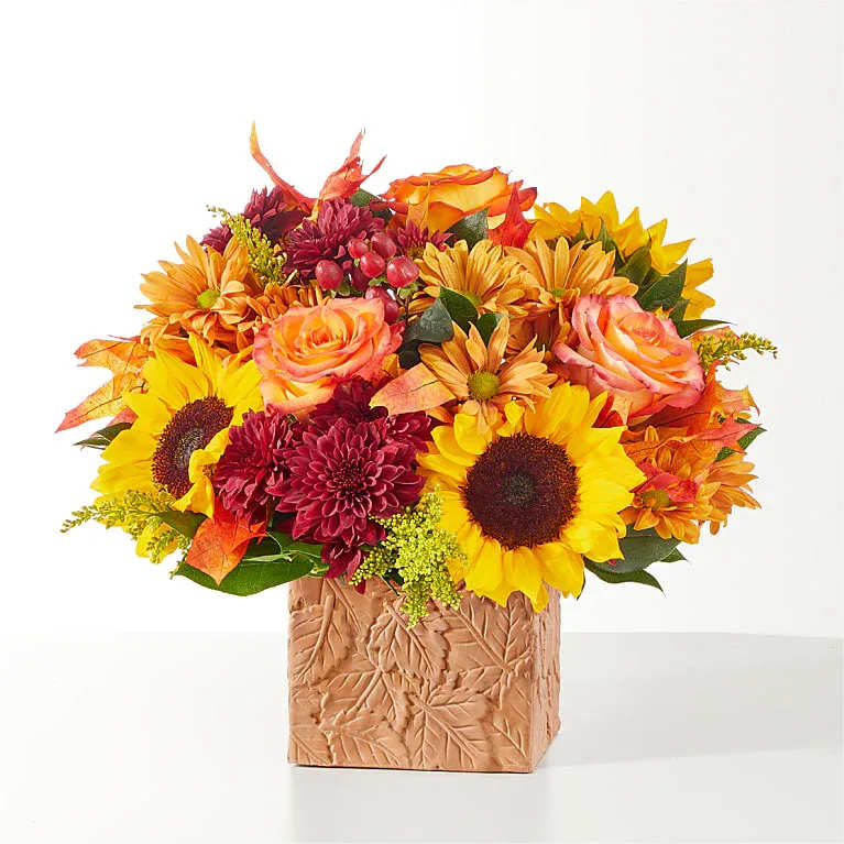 Autumn bouquet of sunflowers, roses, and mums in a leaf-patterned vase